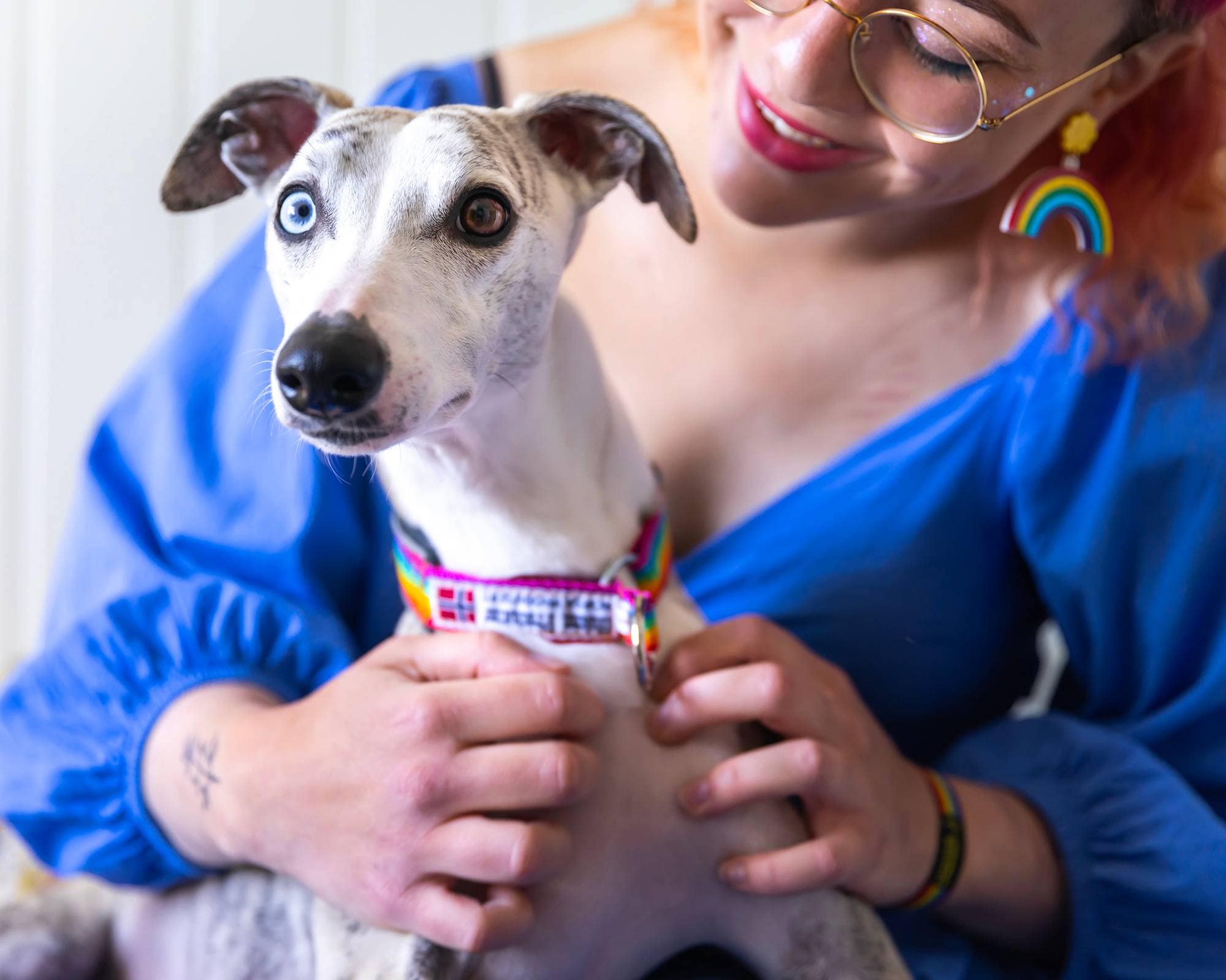 Jeanette (25) smiler mens hun koser med hunden Bambi. Bambi har to forskjellige øyefarger og et halsbånd med Pride-farger.