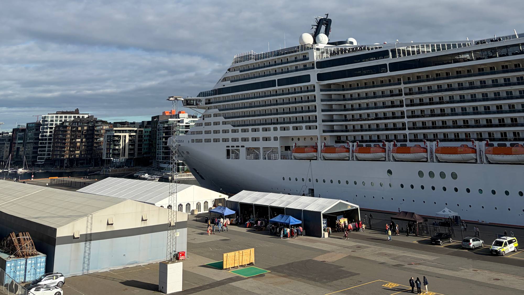 Et stort cruiseskip ligger til kai ved en terminal under en delvis skyet himmel. (Bildebeskrivelsen er laget av en KI-tjeneste)