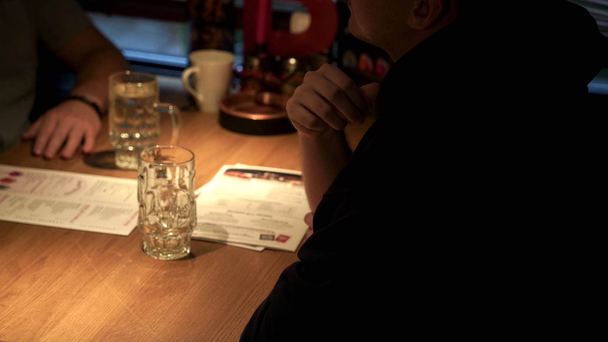 En anonym mann sitter ved et bord med vannglass foran seg og snakker med en journalist. Ser bare hånda og skulderen.