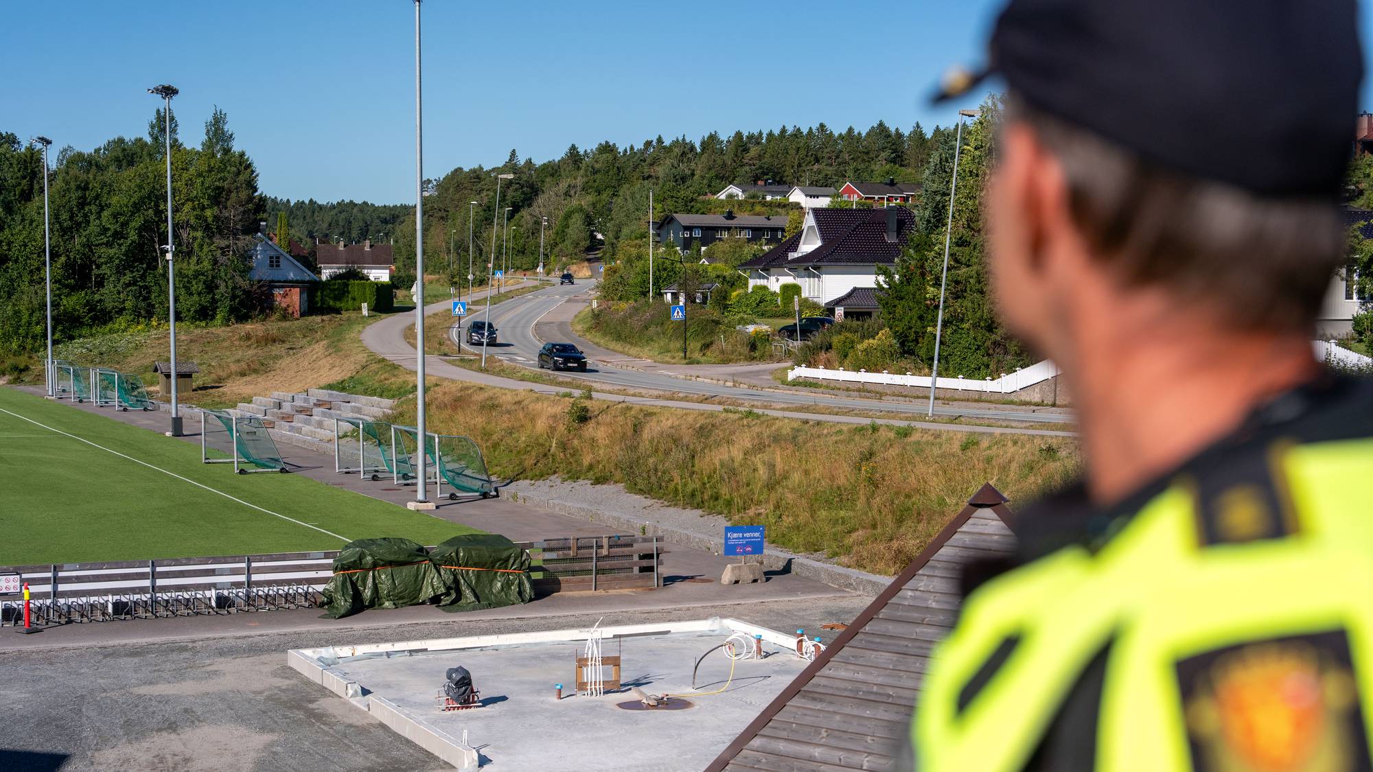 Politimann ses bakfra der han skuer mot trafikkert vei i nabolag ved skole. 