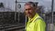Knut Røsrud / NRK En mann står foran et gjerde ved en jernbanestasjon. Han har på seg en lys gul arbeidsdrakt med refleksdetaljer. Bakgrunnen viser jernbanespor og en delvis skyet himmel. Det er tydelig at han har en arbeidsrelatert rolle i nærheten av jernbanen. (Bildebeskrivelsen er laget av en KI-tjeneste)