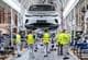 DAVID HECKER / AFP / NTB Bildet viser arbeidere i en bilfabrikk som er i ferd med å montere elbilen Volkswagen ID.4. Flere personer i gule vester jobber med ulike oppgaver langs produksjonslinjen. En hel bil henger oppe på en monteringskran, mens andre arbeidere følger med på prosessen. Omgivelsene er preget av et moderne fabrikklokale med industrielt utstyr og organisert arbeidsplass. (Bildebeskrivelsen er laget av en KI-tjeneste)