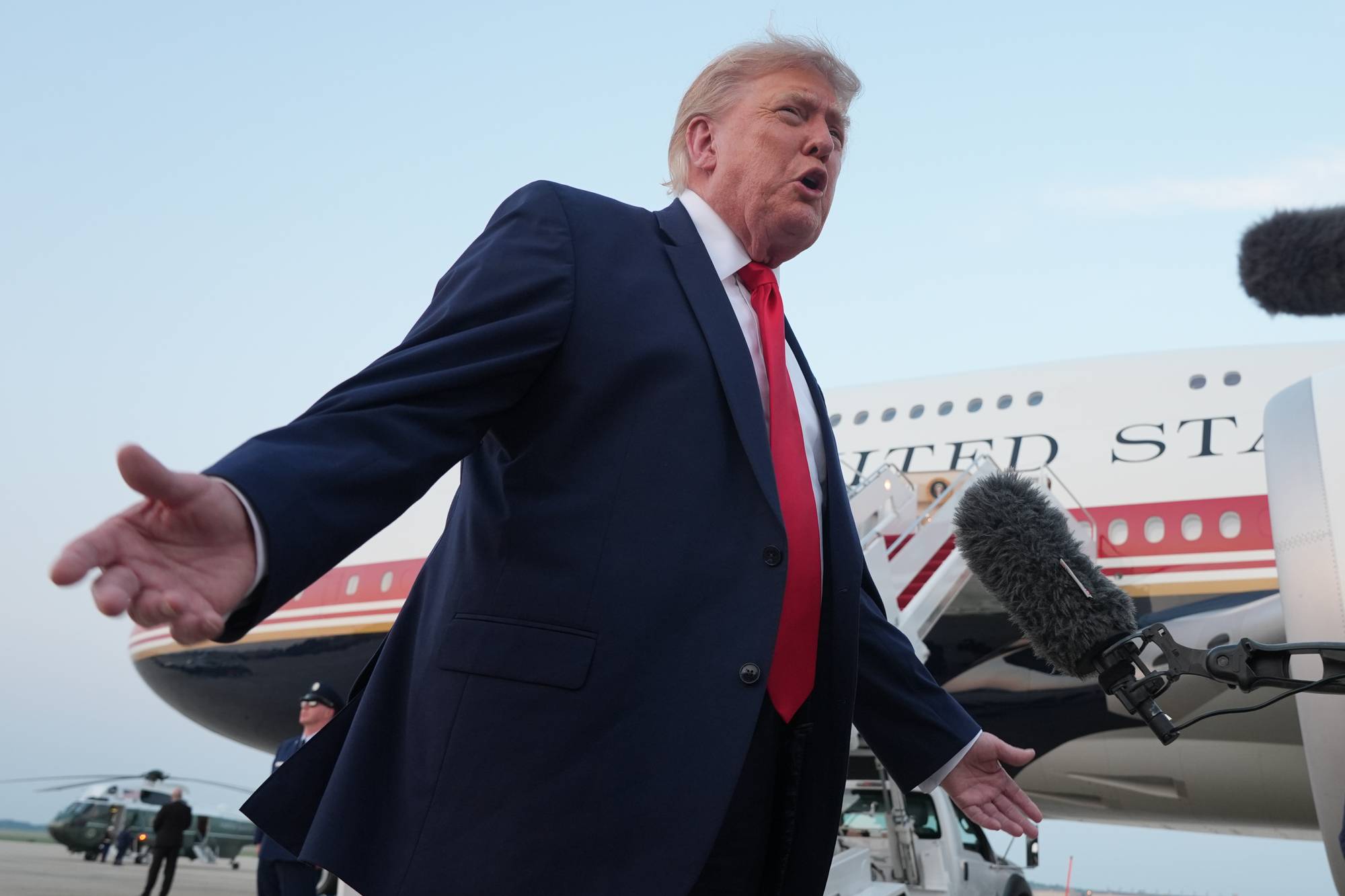 Donald Trump snakker foran en mikrofon med et fly i bakgrunnen. (Bildebeskrivelsen er laget av en KI-tjeneste)
