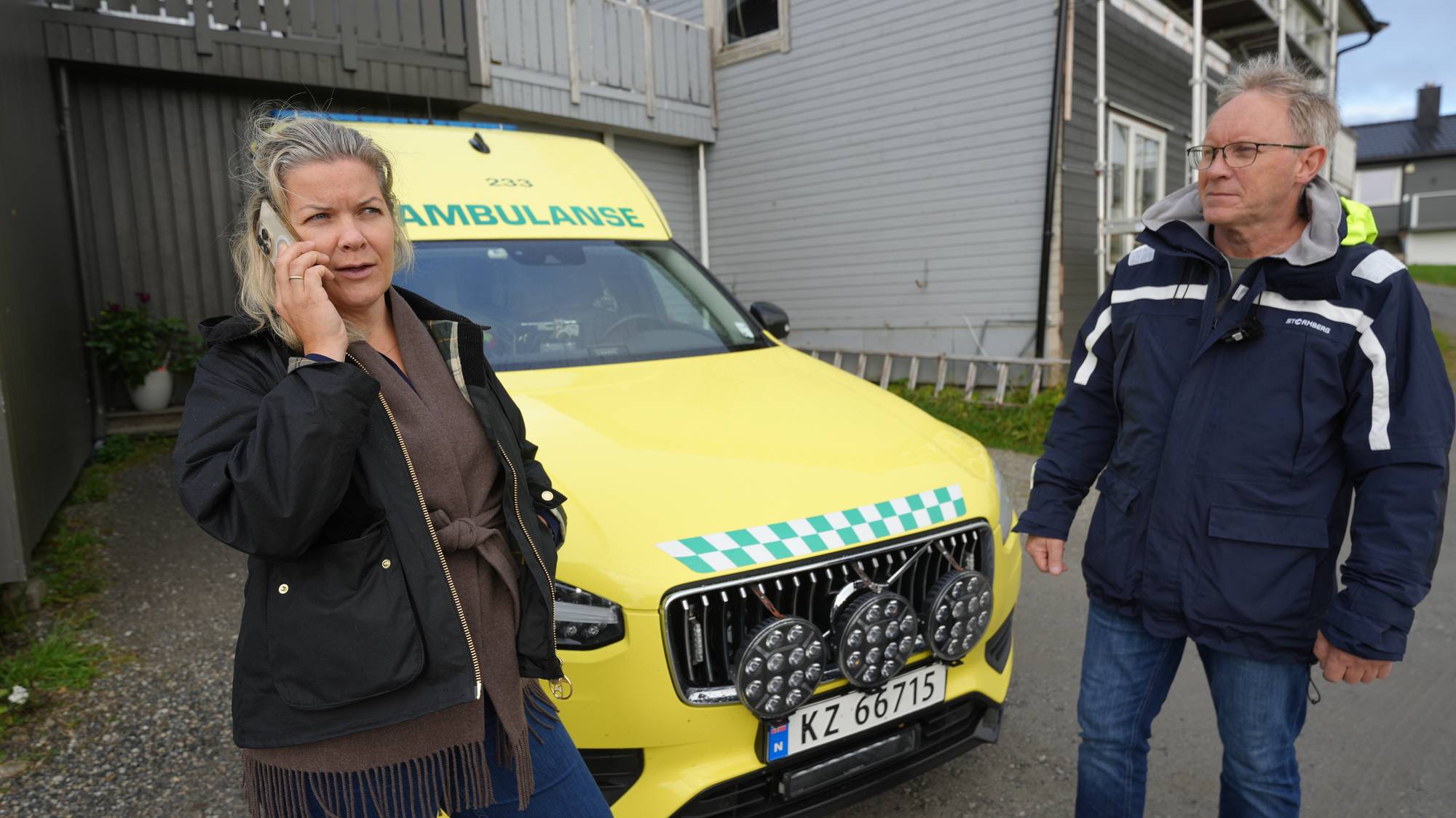 Kvinne snakker i mobiltelefon foran en ambulanse, ved siden av står en mann. (Bildebeskrivelsen er laget av en KI-tjeneste)