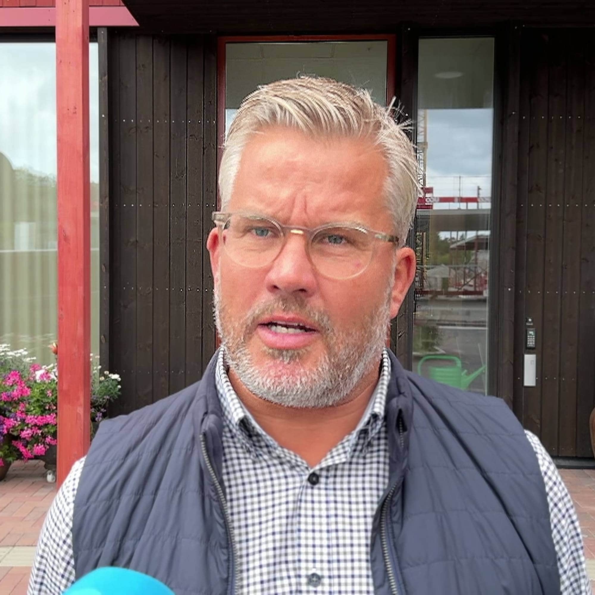 En mann med briller og skjegg står utendørs foran en bygning med mørk kledning. (Bildebeskrivelsen er laget av en KI-tjeneste)