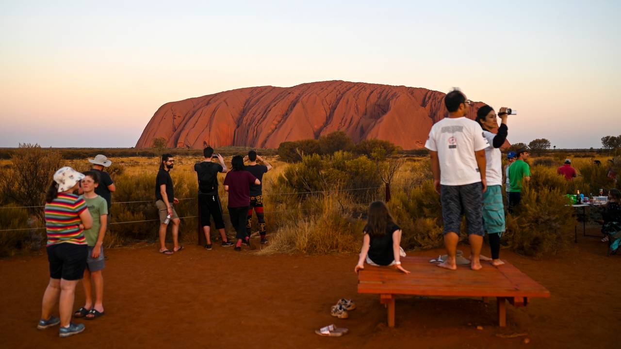 Turister ser på det karakteristiske fjellet Uluru i Australia.