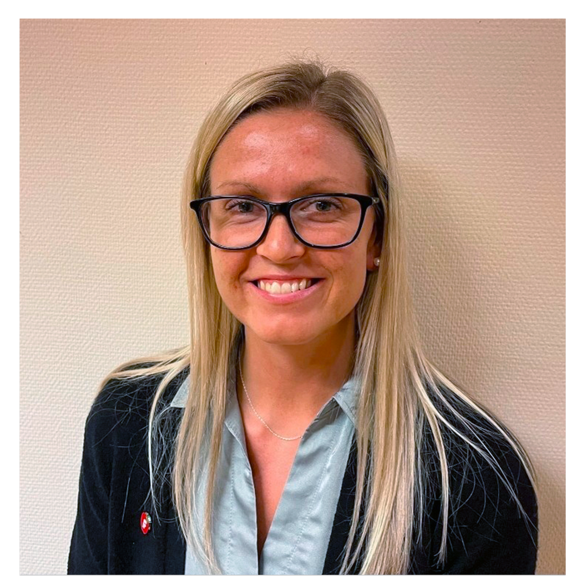 Dame med blondt hår, briller og formelt kledd med skjorte og jakke. Frp-pin på jakka.