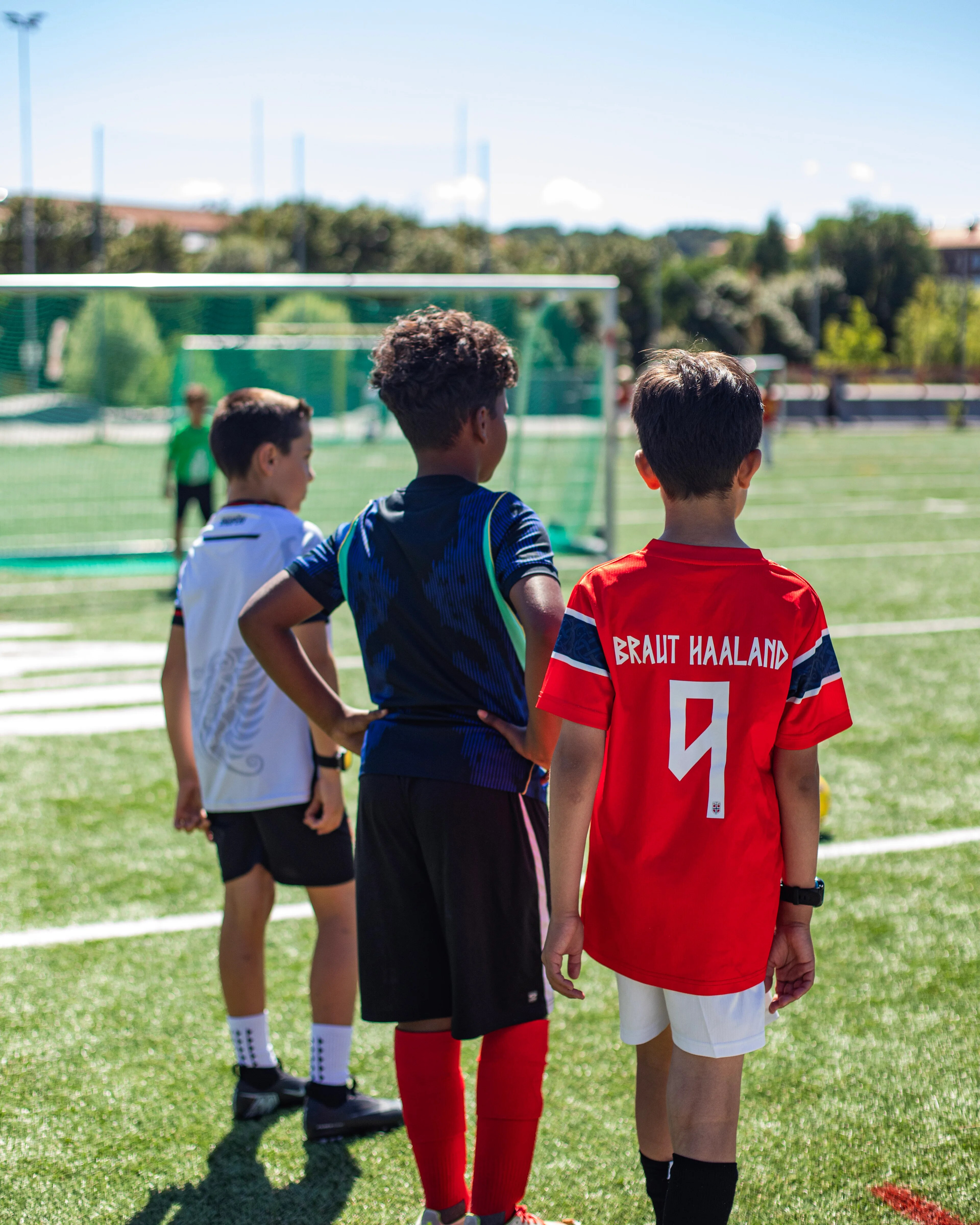 Bildet viser tre gutter som står på en fotballbane. Gutten som står nærmest kameraet har på seg en en Haaland-drakt.