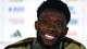 HARRY HOW / GETTY IMAGES NORTH AMERICA,NTB Alphonso Davies smiler under en pressekonferanse med uklare sponsorlogoer i bakgrunnen. (Bildebeskrivelsen er laget av en KI-tjeneste)
