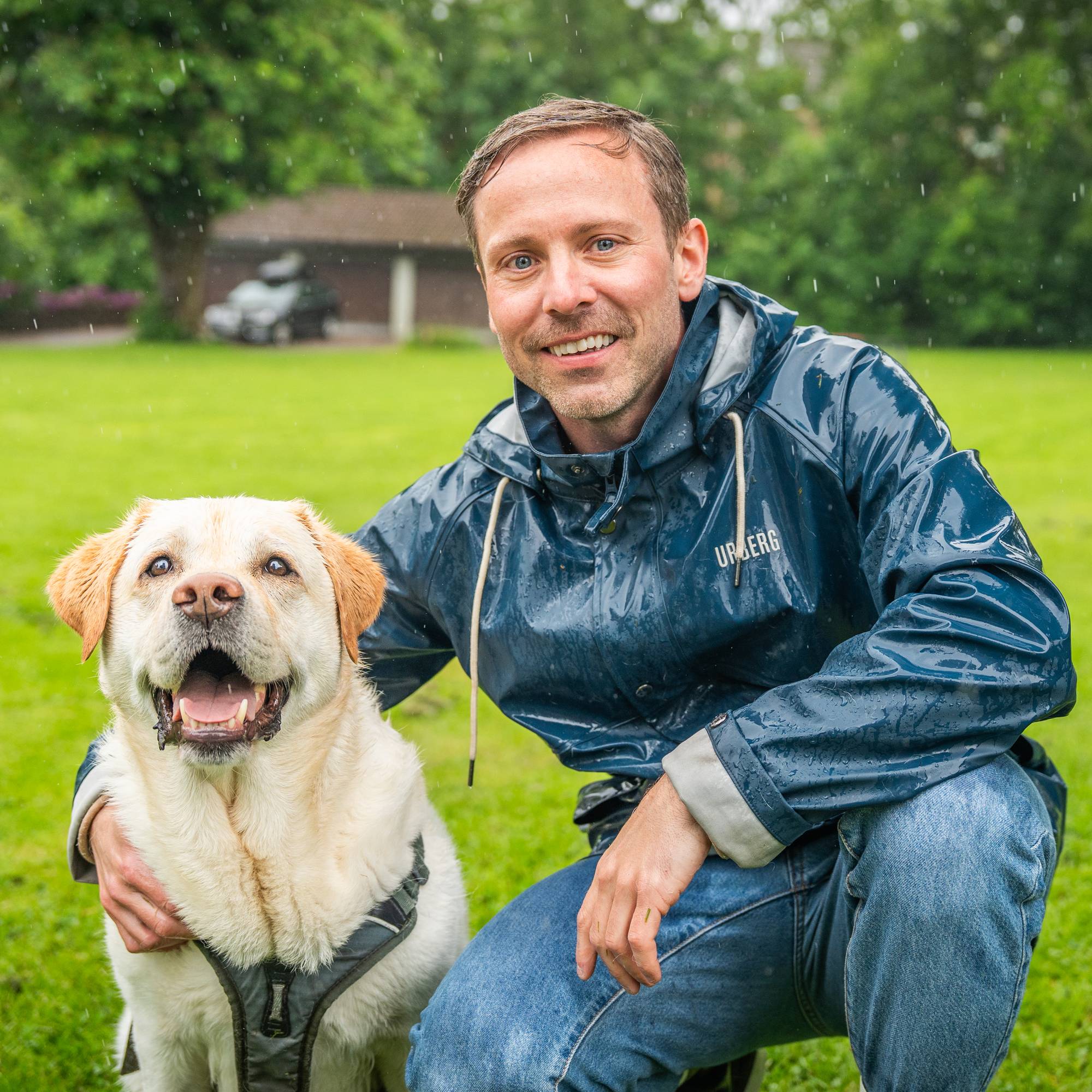 En hvit hund og en mann i regnjakke