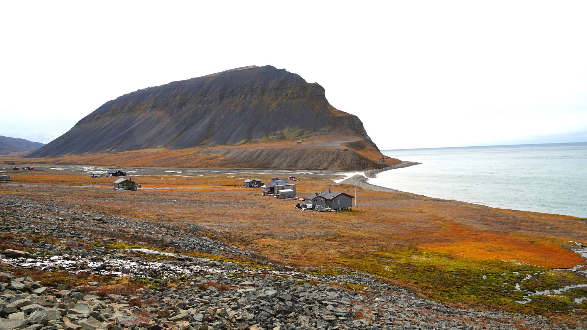 Hytter på en slette, hav og fjell i høstlige farger. 