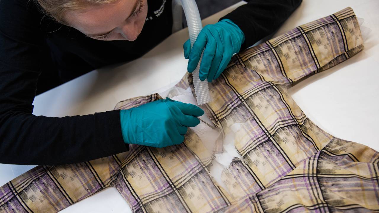 Tekstilkonservator Signe Thøgersen bruker dampmaskin for å rette ut stoffet på kjolen fra Ørnerovet som har ei svær flenge over brystet.