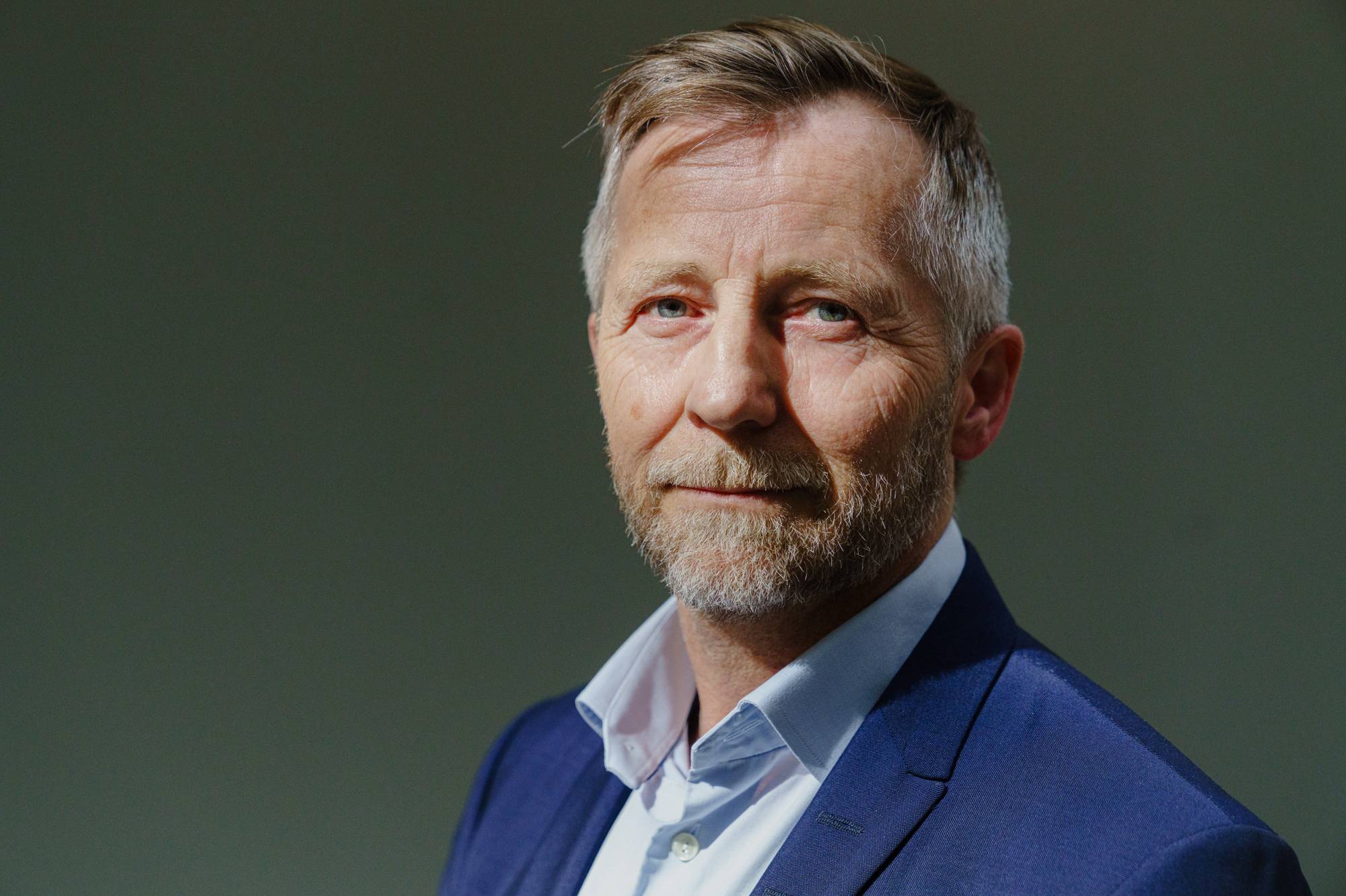 Portrett av en mann i dress med skjegg og blond-grått hår som ser mildt i kamera