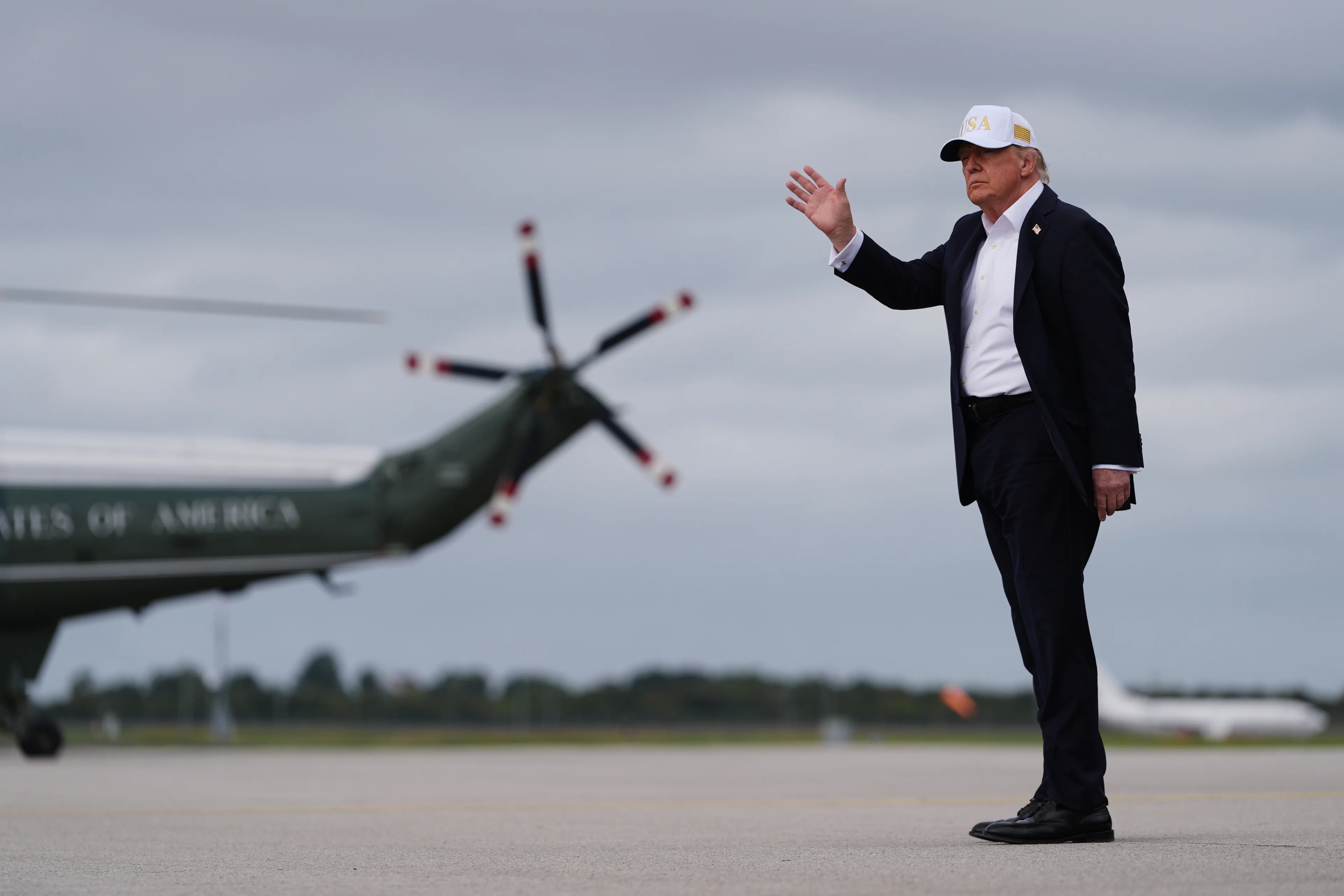 Donald Trump vinker foran et helikopter på en flyplass. (Bildebeskrivelsen er laget av en KI-tjeneste)