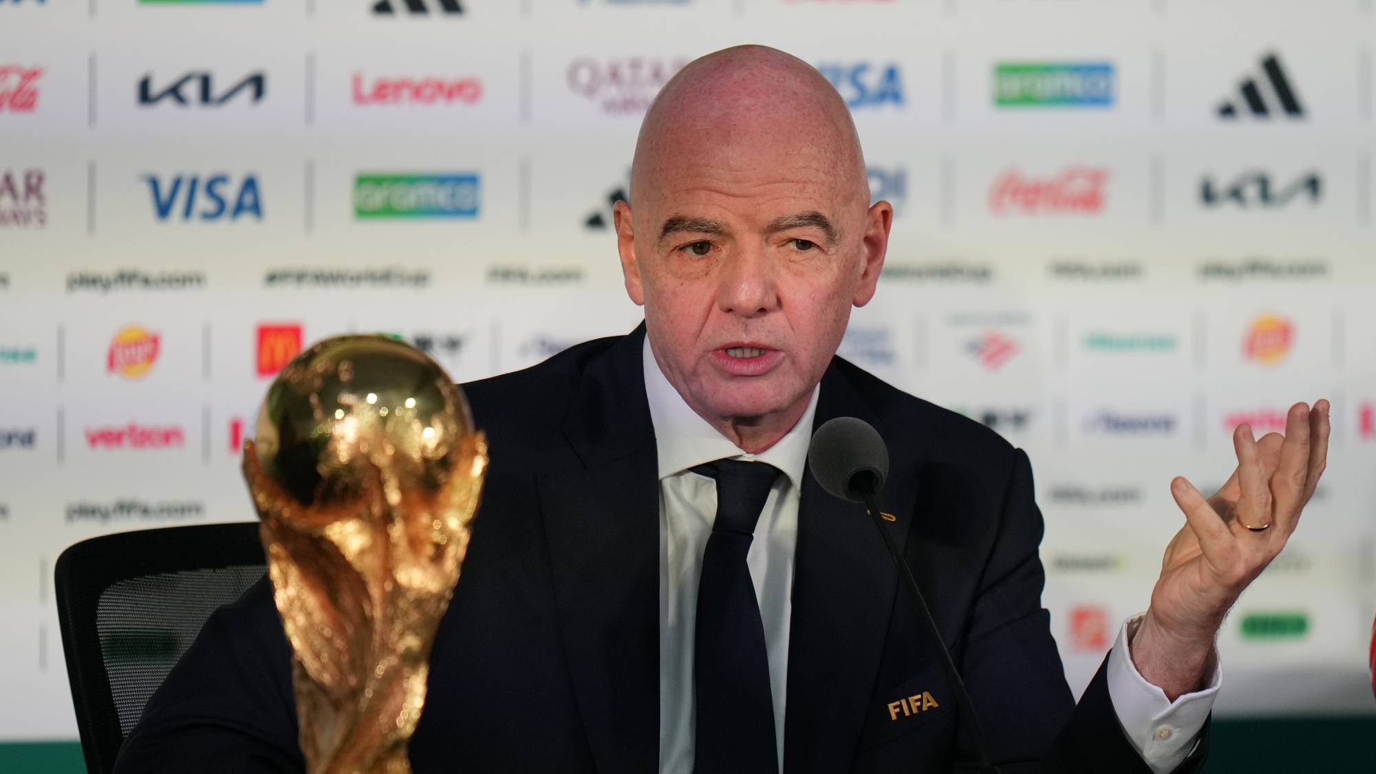 FIFA-president Gianni Infantino snakker foran VM-trofeet under en pressekonferanse. (Bildebeskrivelsen er laget av en KI-tjeneste)