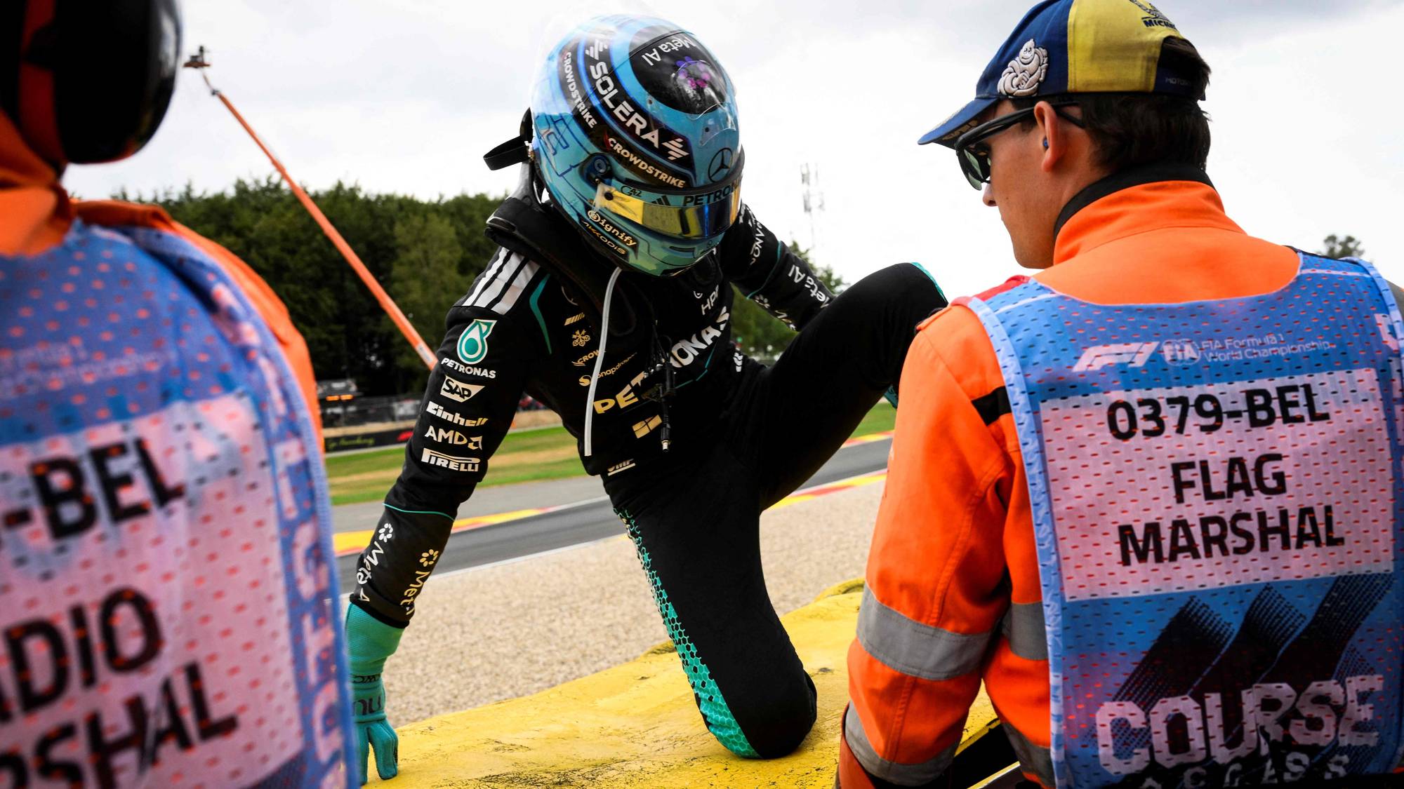 Formel 1-fører klatrer over autovernet på racerbanen assistert av banemanskaper. (Bildebeskrivelsen er laget av en KI-tjeneste)