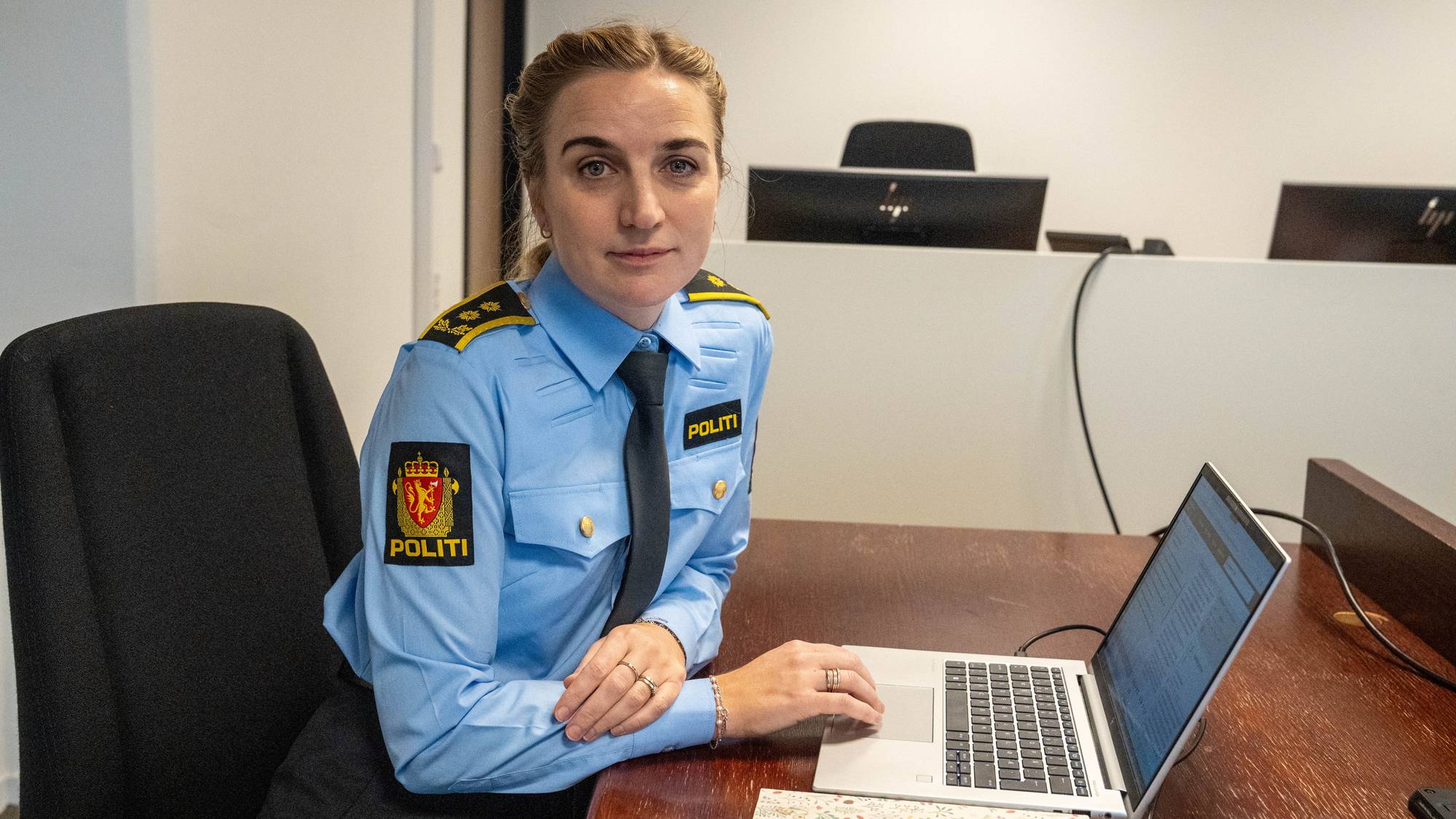 En kvinne iført politiuniform sitter ved en laptop på et kontor