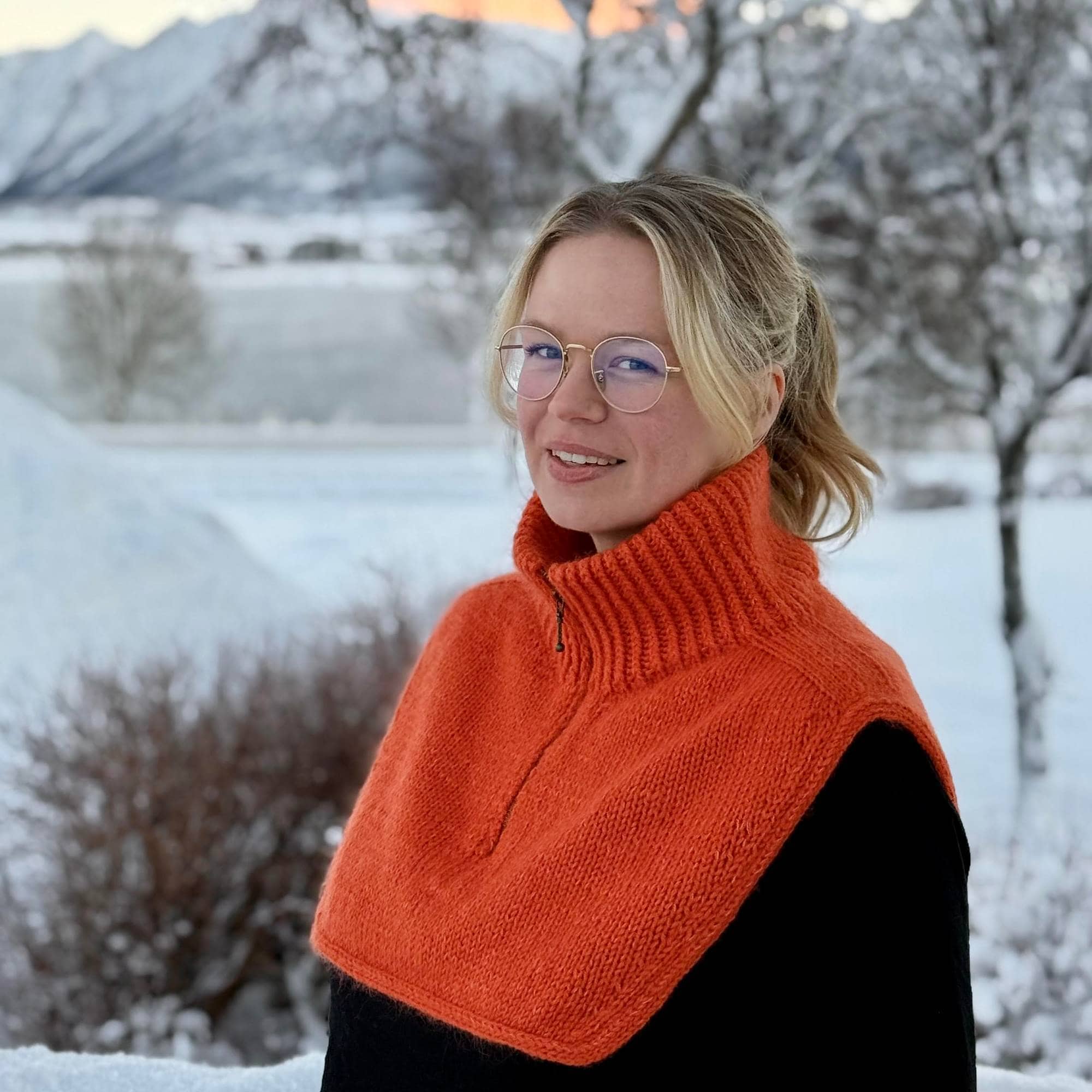 Kvinne står ute om vinteren med sort jakke og en strikket krage.