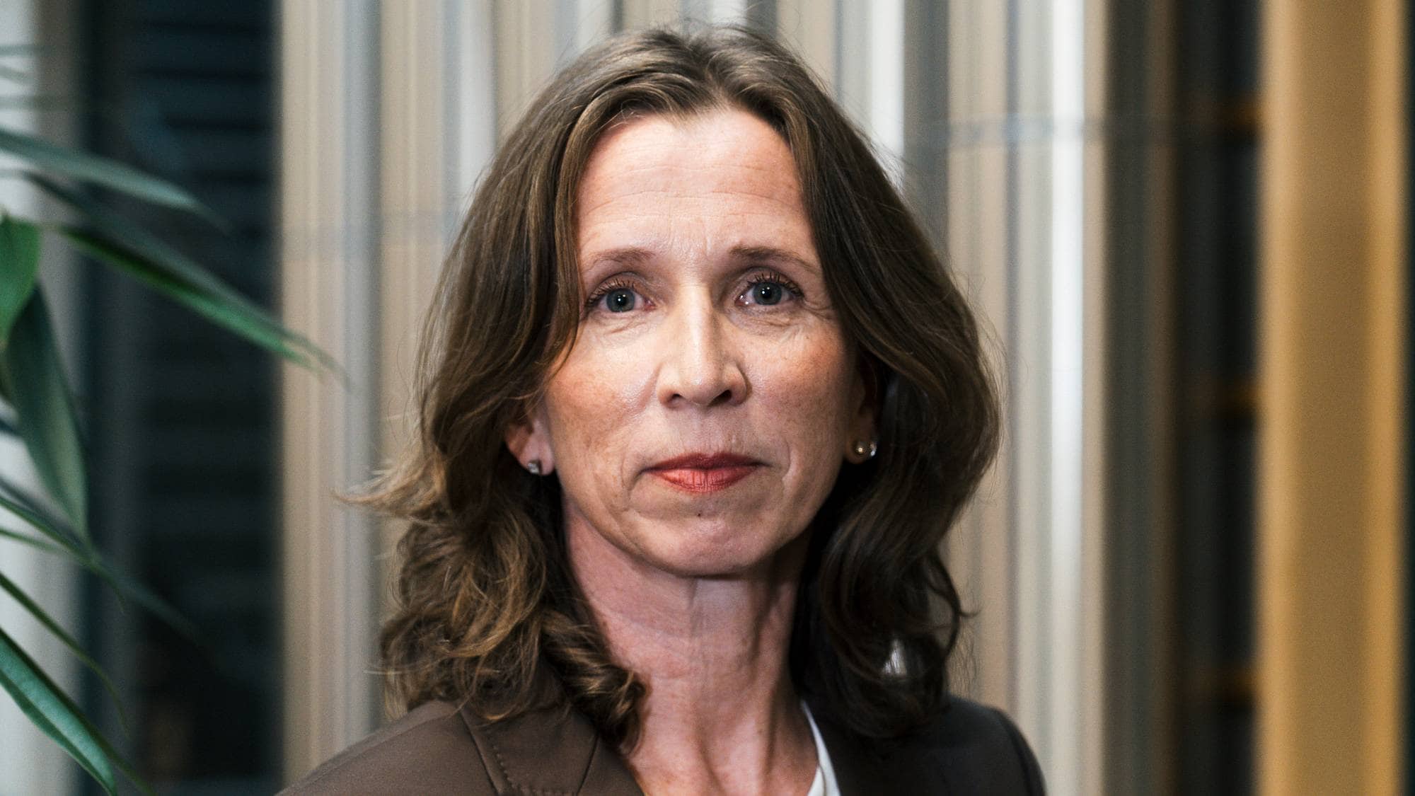 Portrett av kvinne med brunt hår i en brun dressjakke over en hvit topp. 