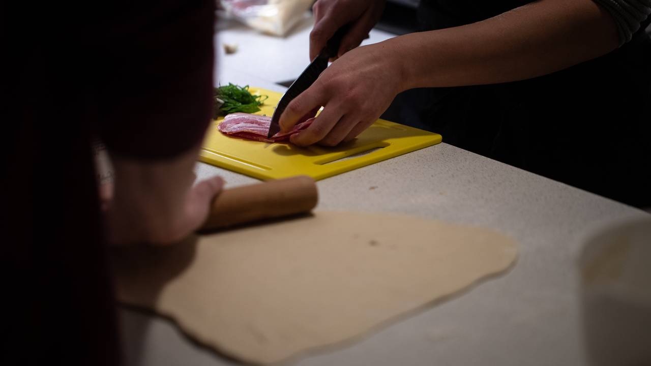William har er lite kjevle han baker ut pizzadeigen med på kjøkkenbenken, mens Tram deler opp baconskiver som skal på pizzaen.