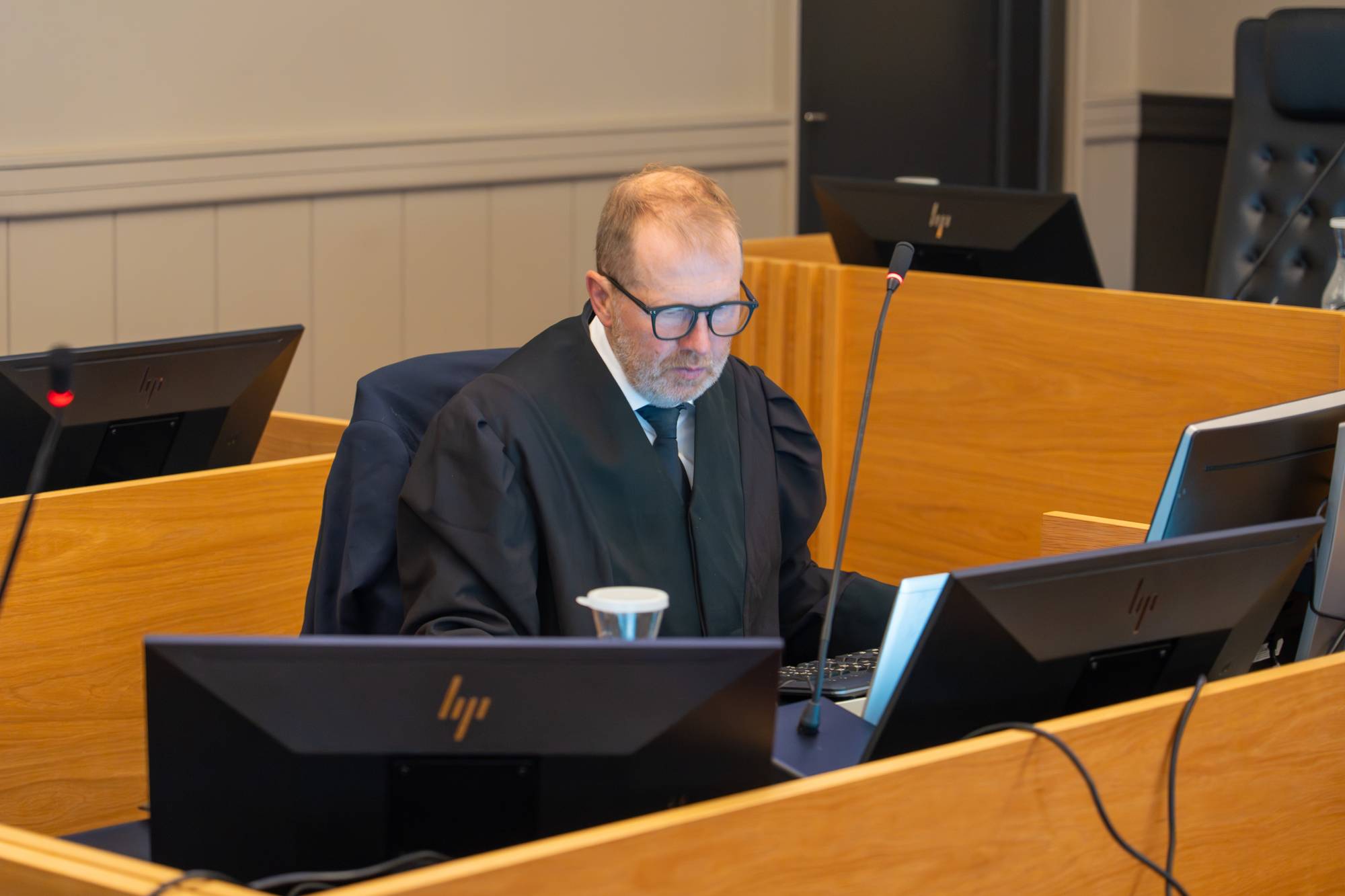 En mann med rettskappe i rettssal ved sin pult med skjermer og mikrofon.