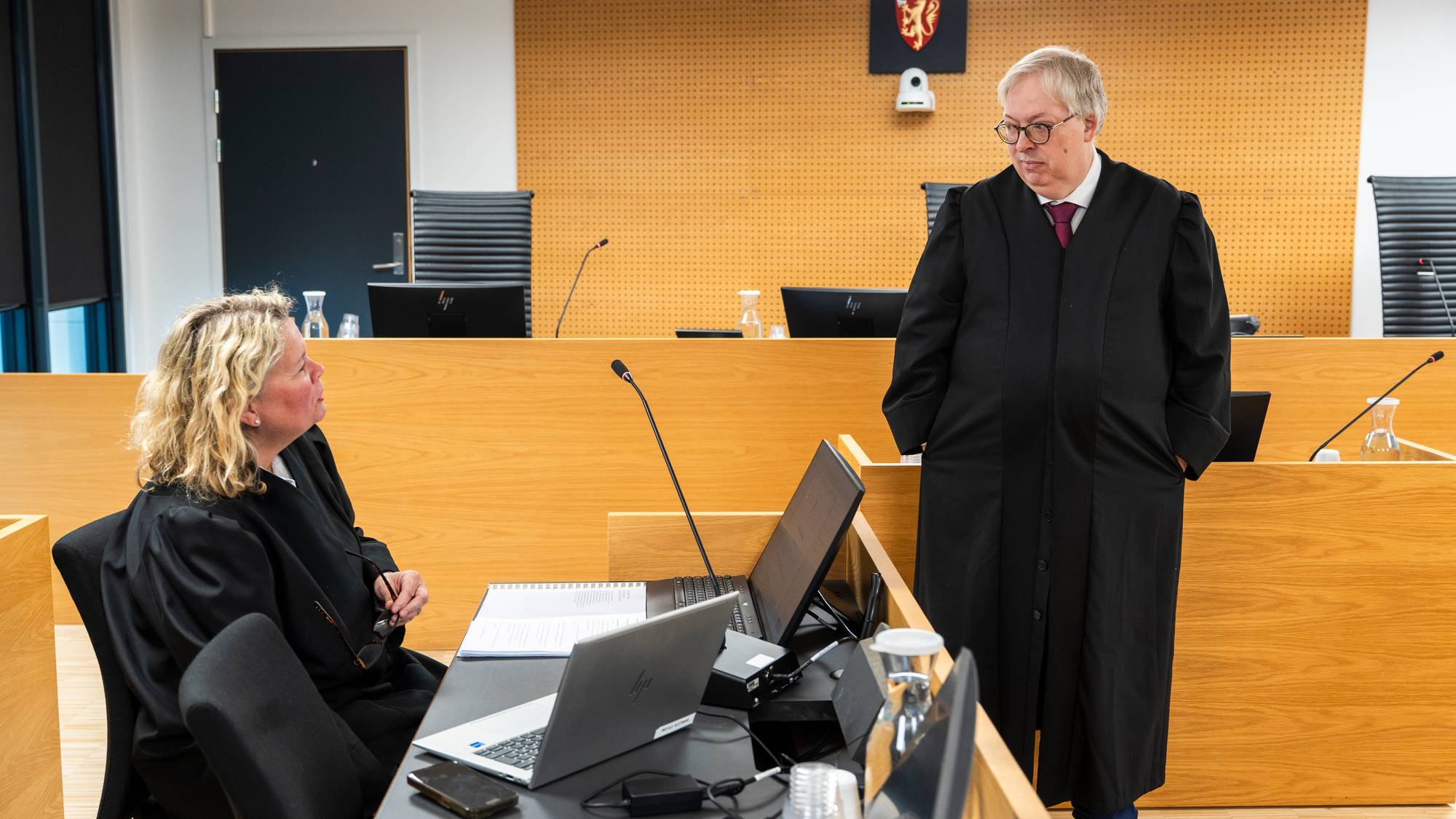 To jurister i kapper snakker sammen i en rettssal. (Bildebeskrivelsen er laget av en KI-tjeneste)