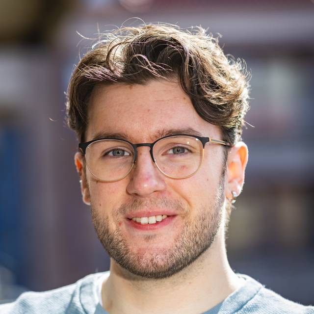 Et portrett av Daniel Restad. Han har brunt, halvkort bølgete hår, blågrønne øyne og smiler pent til kamera.