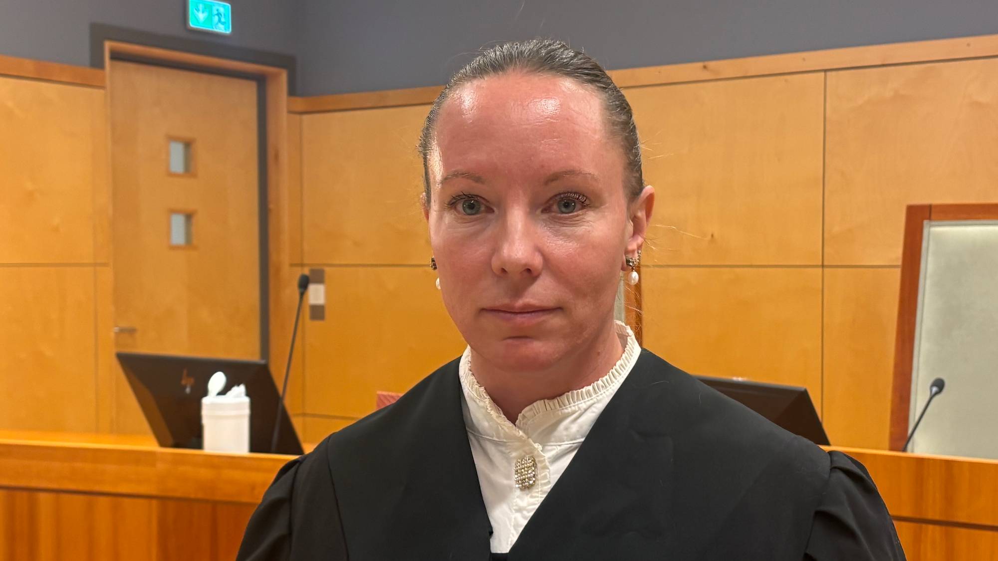 Kvinne i svart advokatkappe står i en rettssal. (Bildebeskrivelsen er laget av en KI-tjeneste)