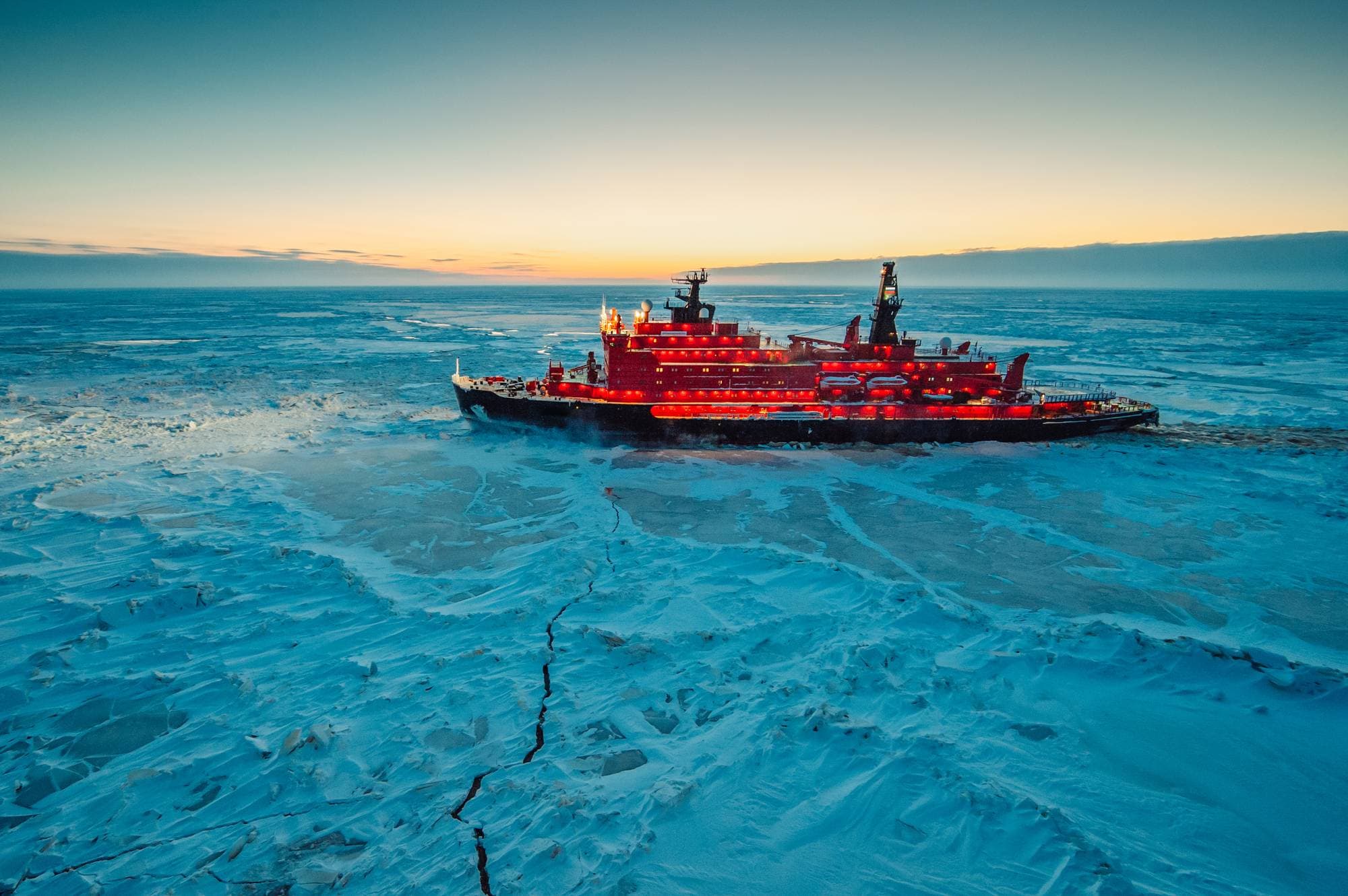 Rød isbryter navigerer gjennom et islagt arktisk landskap ved solnedgang. (Bildebeskrivelsen er laget av en KI-tjeneste)