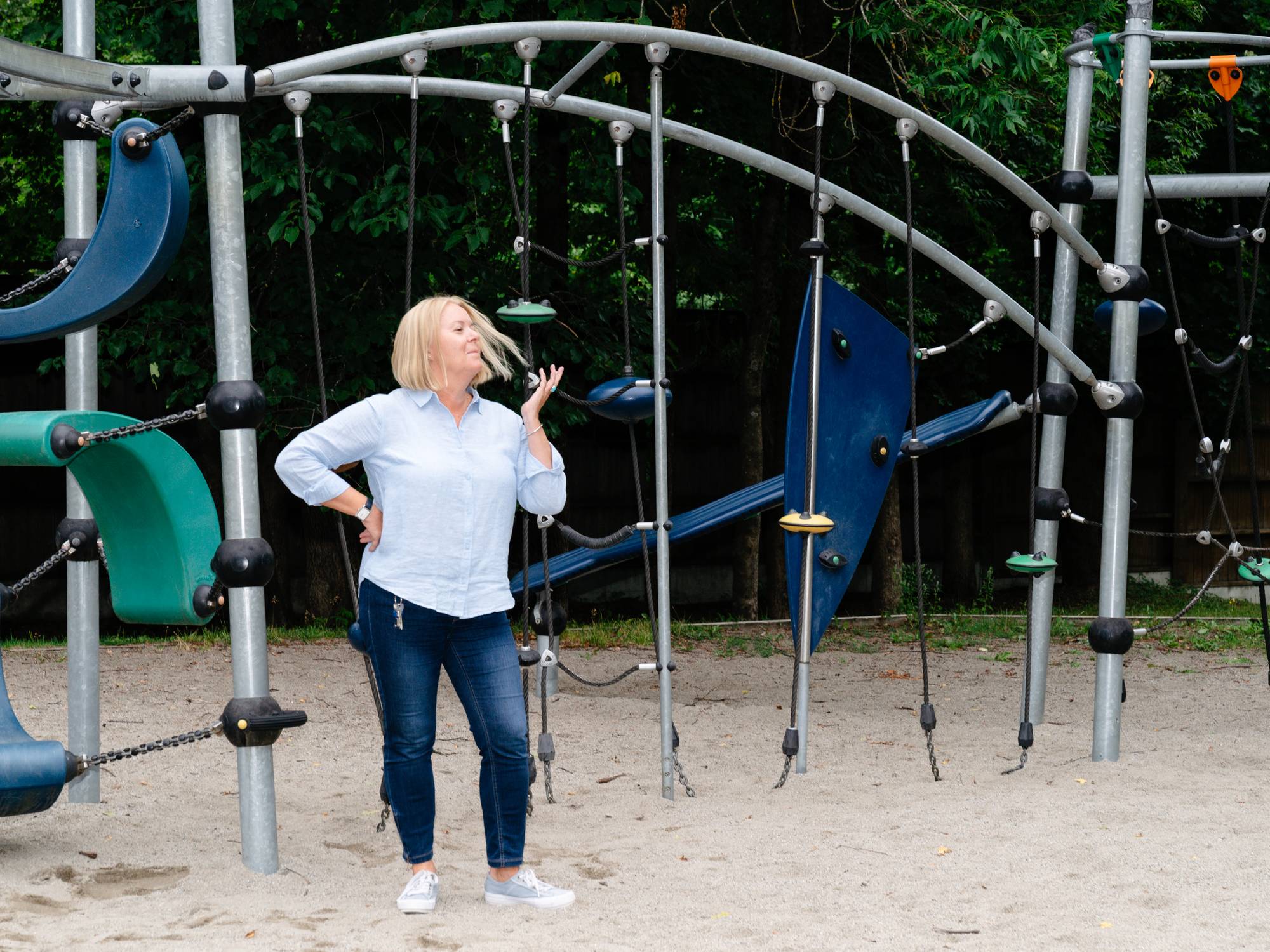 Kvinne står i en lekeplass med klatrestativ av metall i bakgrunnen. (Bildebeskrivelsen er laget av en KI-tjeneste)