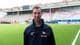 Foto: Fredrikstad Fotballklubb Mann med kort, mørkt hår i svart treningsjakke smiler ute på en fotballbane med tom tribune i bakgrunnen.