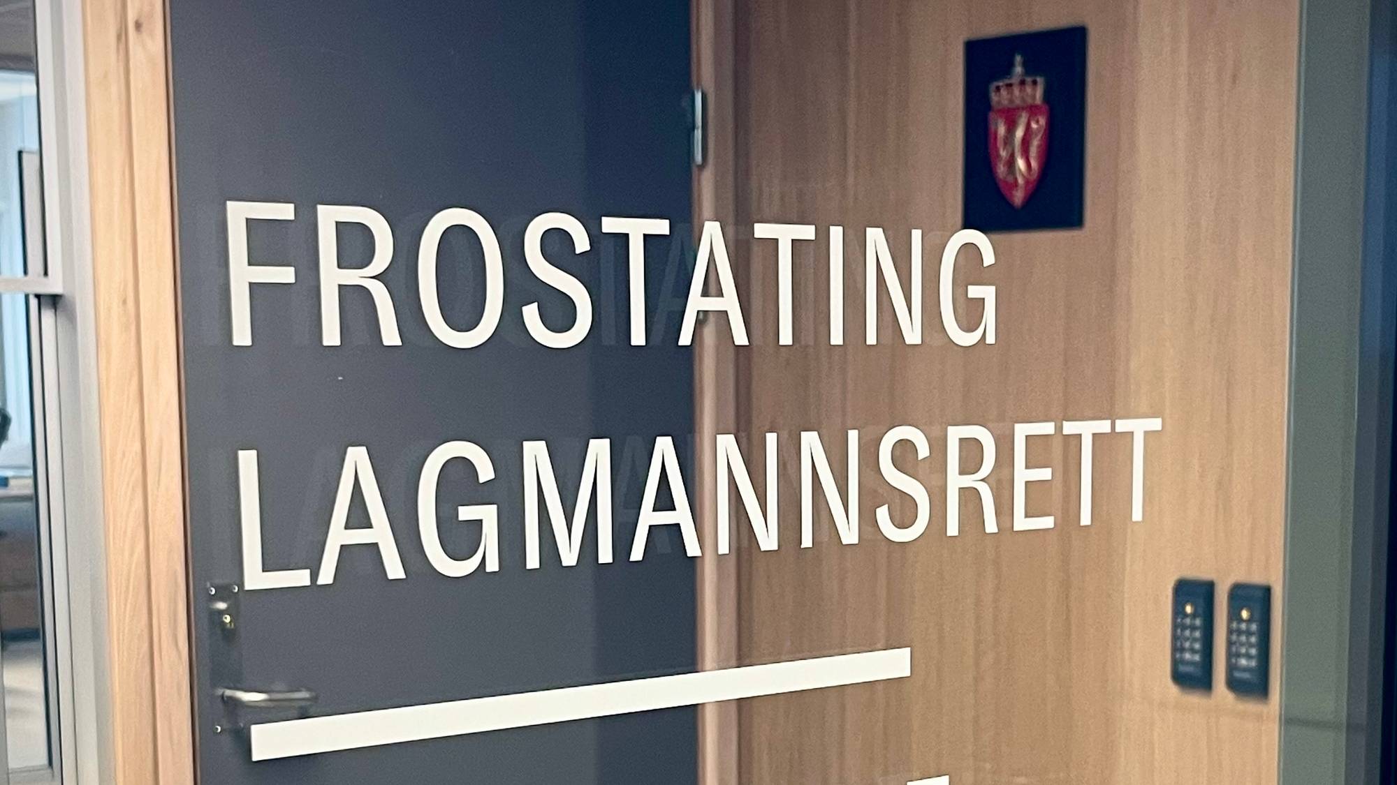 Inngangsdøren til Frostating lagmannsrett og Nordmøre og Romsdal tingrett. Skilt med navnet på rettene er synlig på døren. Til venstre er en skranke. Døren har et dørhåndtak og et elektrisk låsesystem. (Bildebeskrivelsen er laget av en KI-tjeneste)