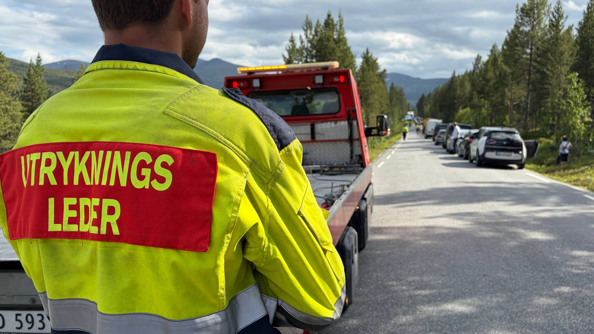 Utrykningsleder ved et bilbergingskjøretøy på en vei med stillestående trafikk og skog. 
