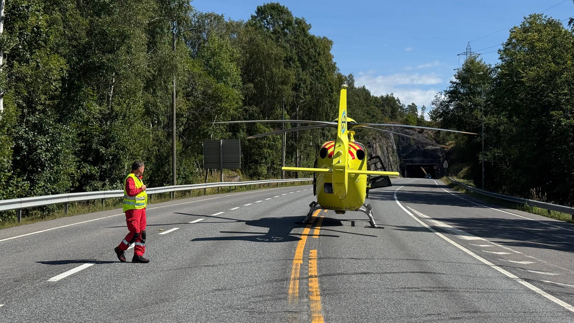 Luftambulanse har landet på en vei, med en person i uniform som går ved siden av helikopteret. (Bildebeskrivelsen er laget av en KI-tjeneste)
