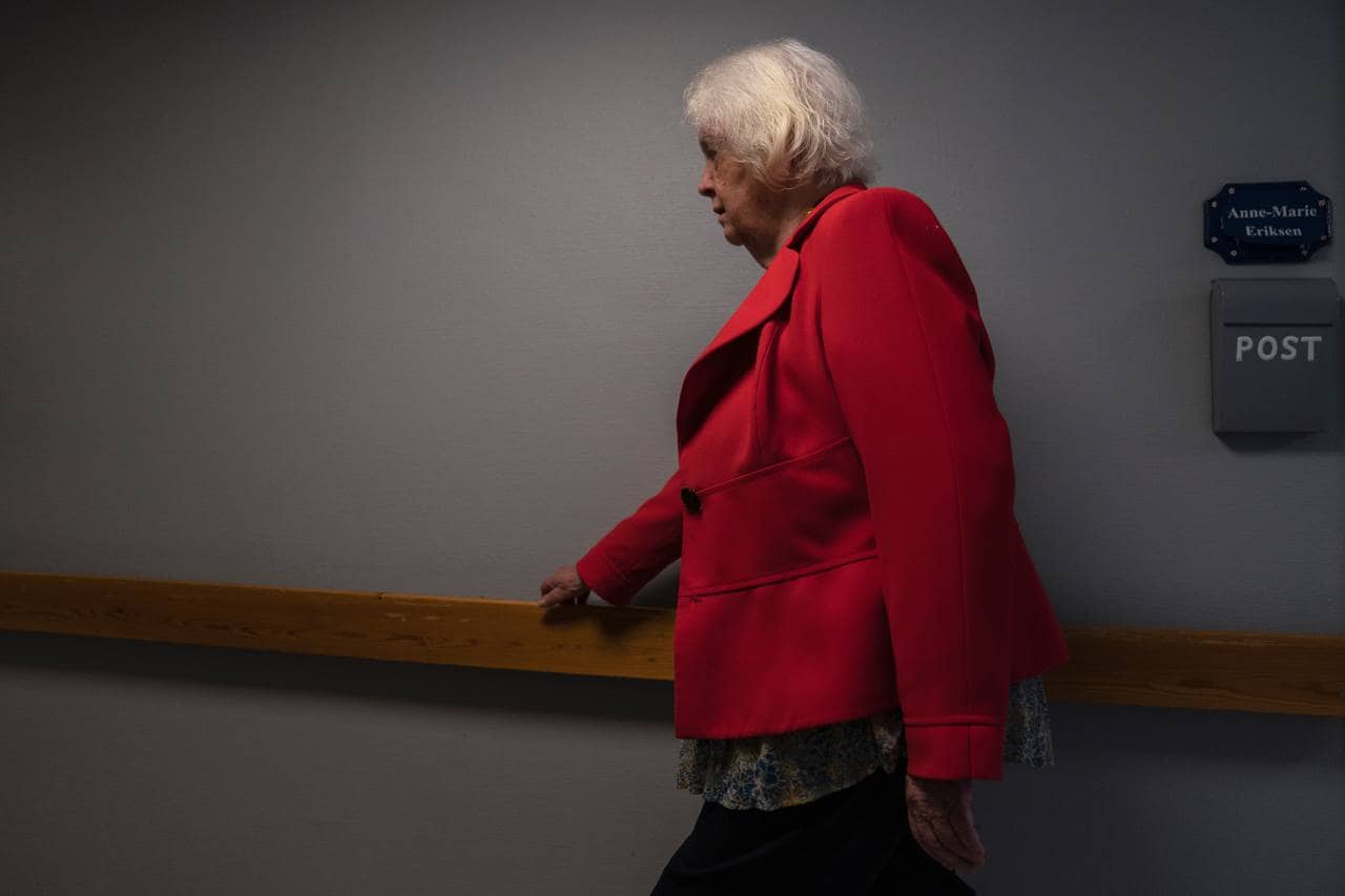 Kvinne i rød jakke går bestemt ned en korridor. Holder seg til gelenderet.