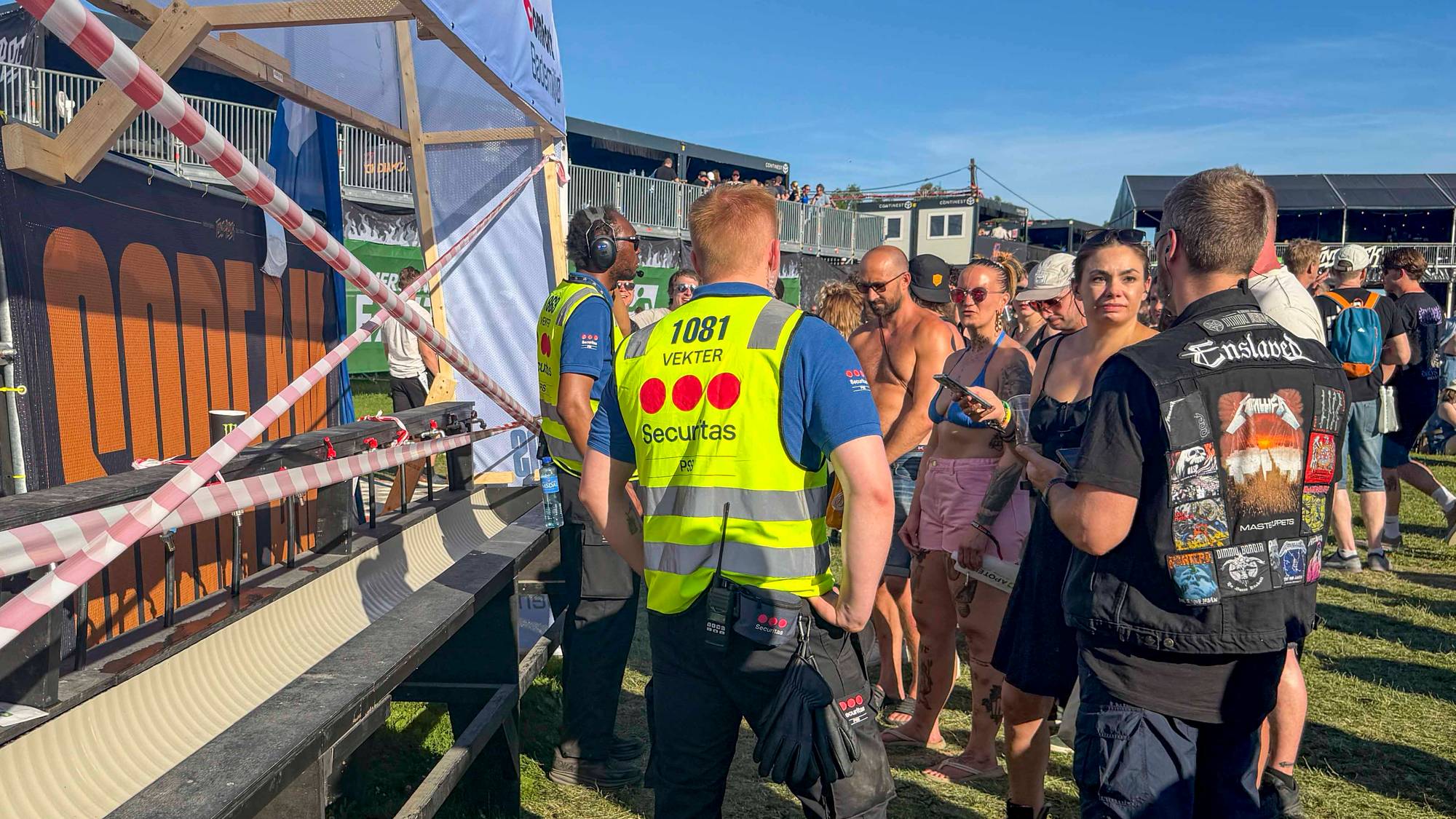 Vektere i refleksvester ved en ølrenne på en festival. Publikummere står i nærheten. (Bildebeskrivelsen er laget av en KI-tjeneste)