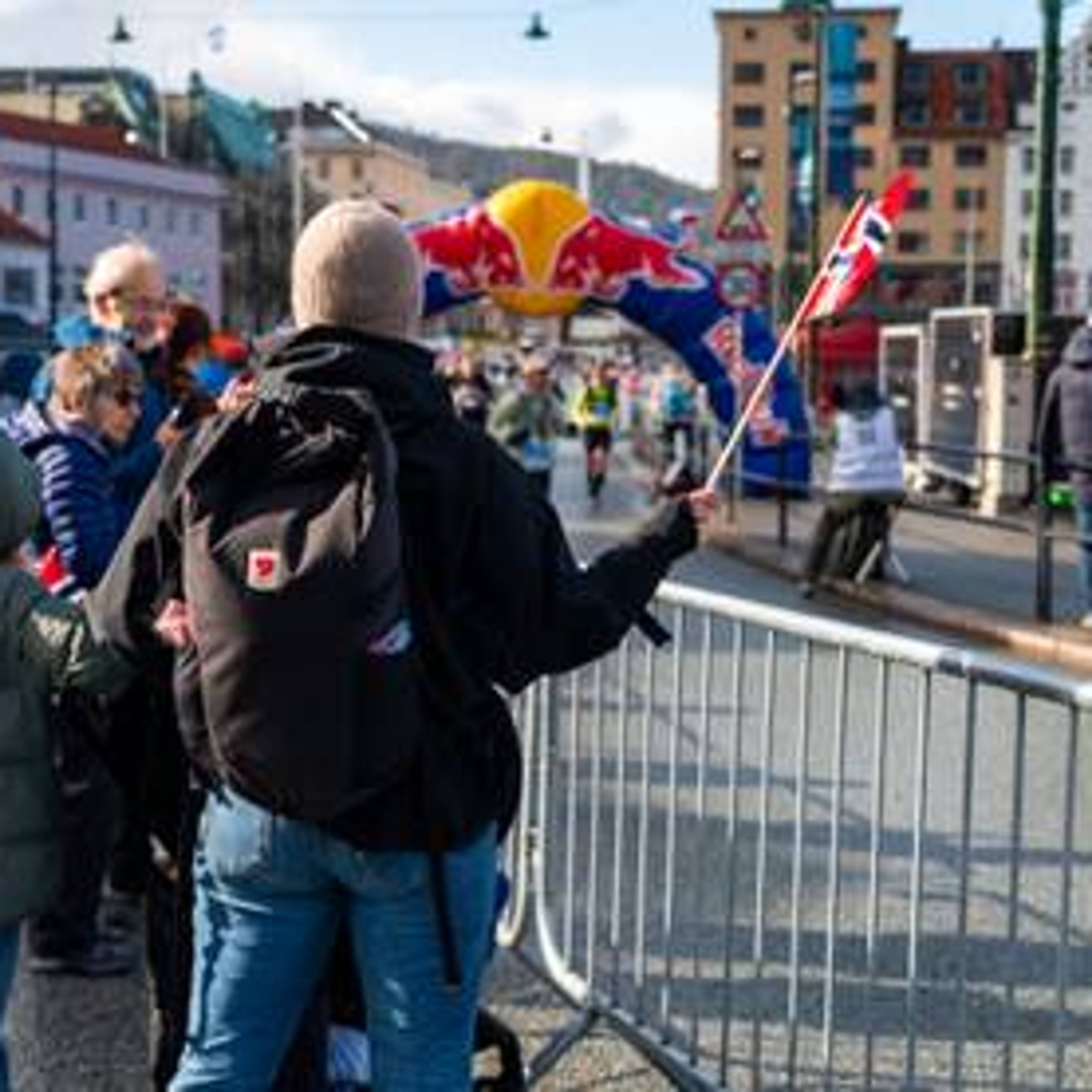 Tilskodar med flagg står med ryggen til langs løypa på Bergen City Marathon.