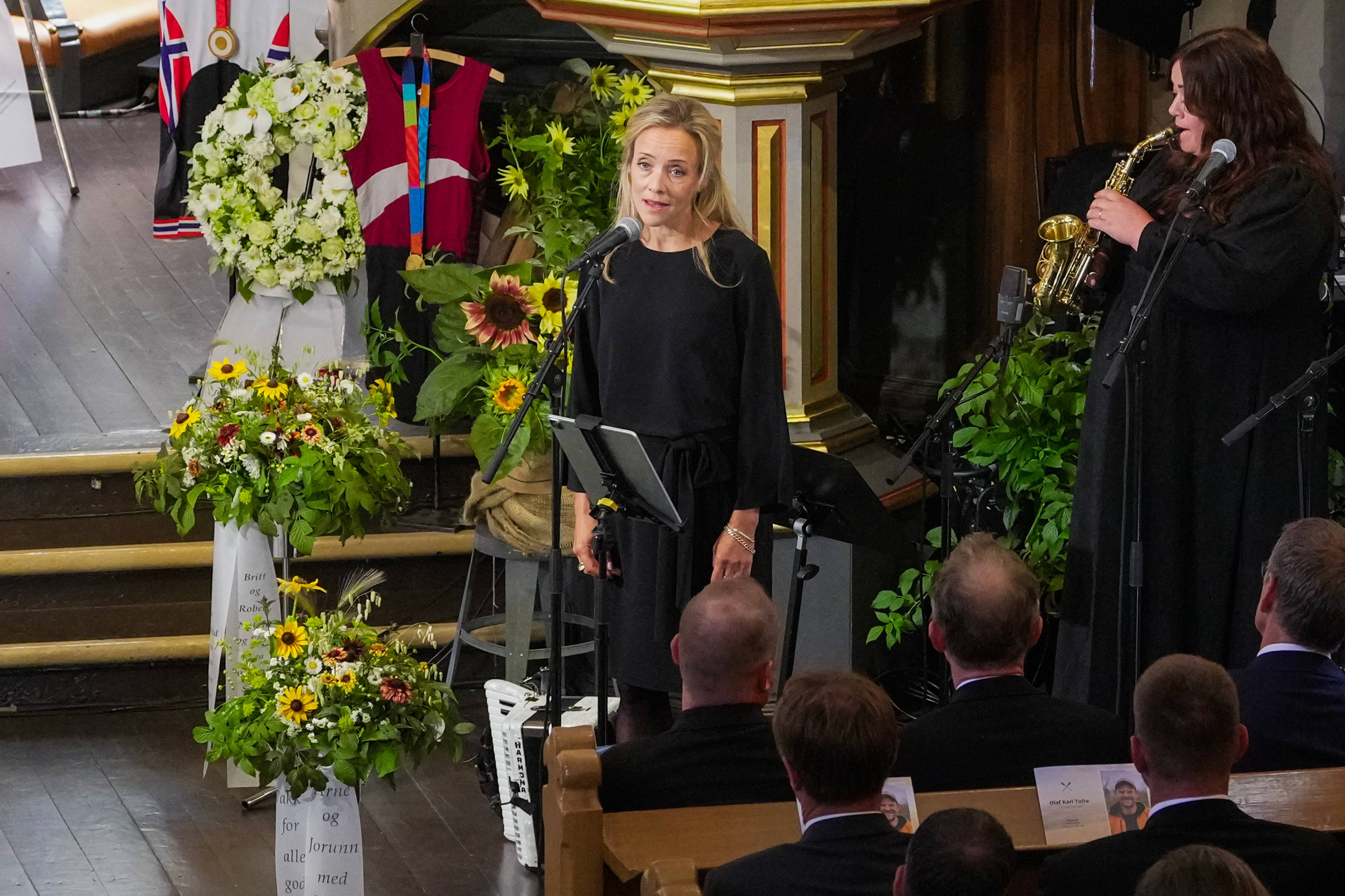 En kvinne synger og en annen spiller saksofon under en begravelse i en kirke.