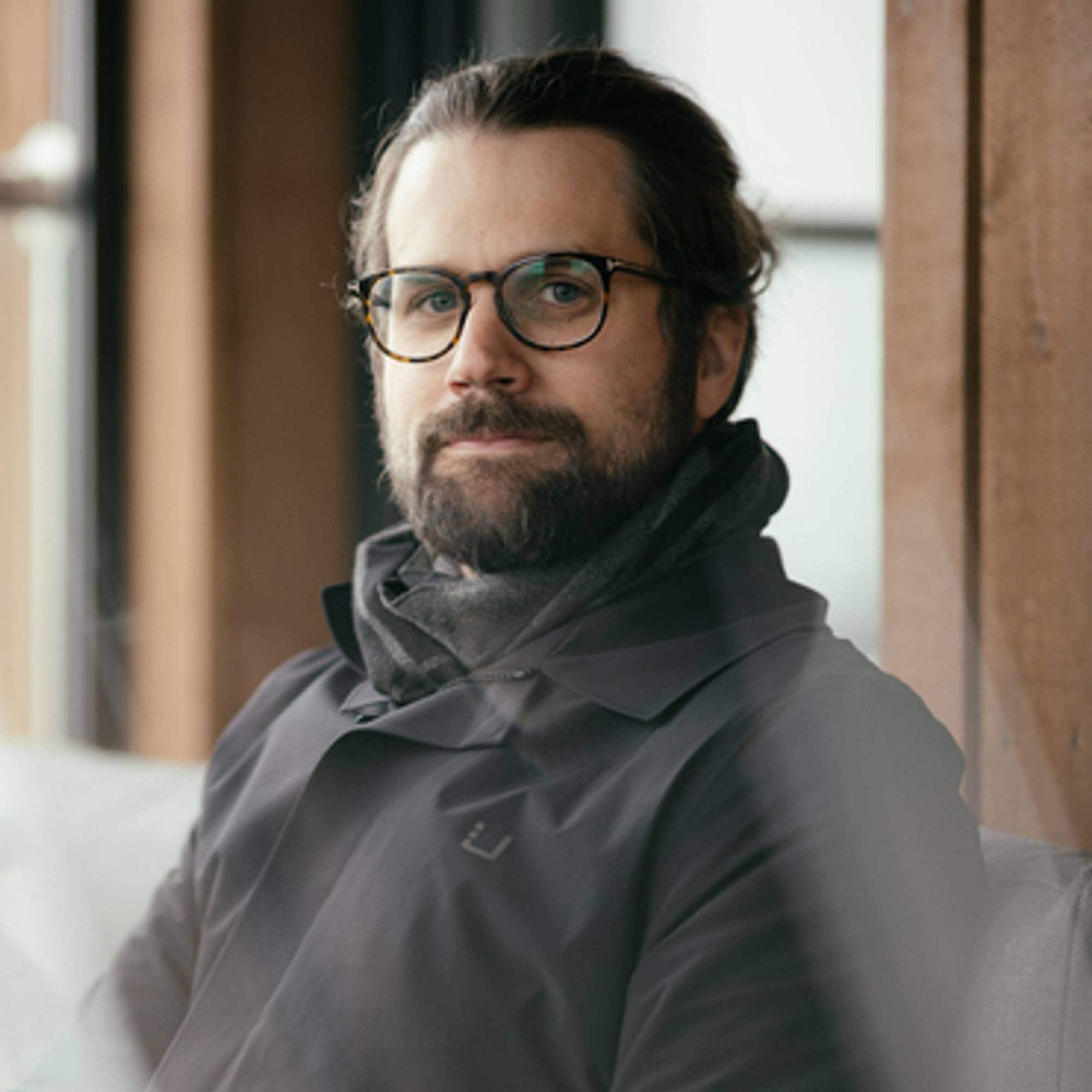 Trygve Børsting har mørkt skjegg og hår. Han har sorte briller og ser rett i kamera med et nøytralt uttrykk. 