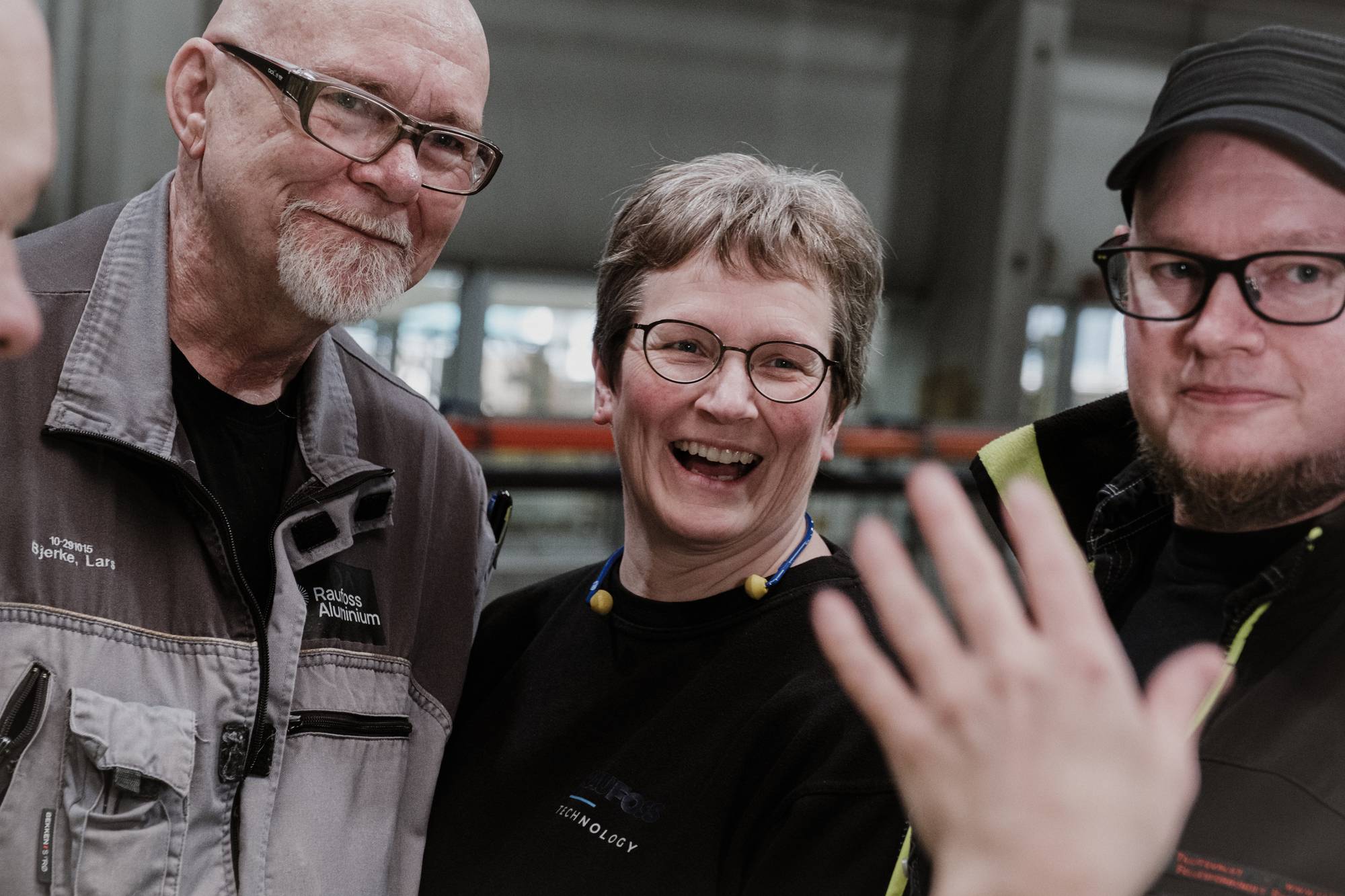 Tre personer står ved siden av hverandre. En smiler, en ler og en har et forsiktig smil
