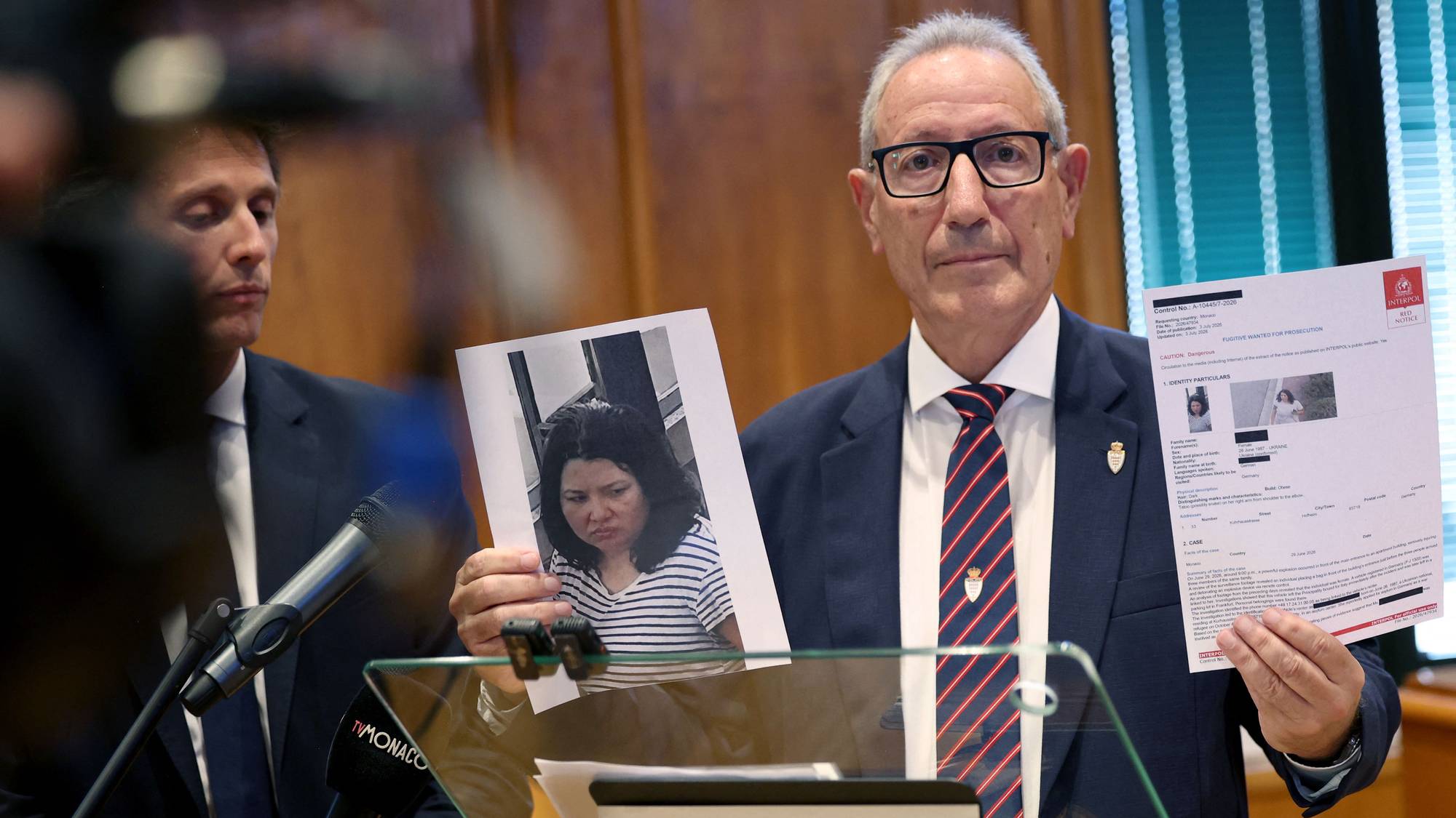 En mann i dress holder opp bilder av en etterlyst kvinne under en pressekonferanse i Monaco. (Bildebeskrivelsen er laget av en KI-tjeneste)