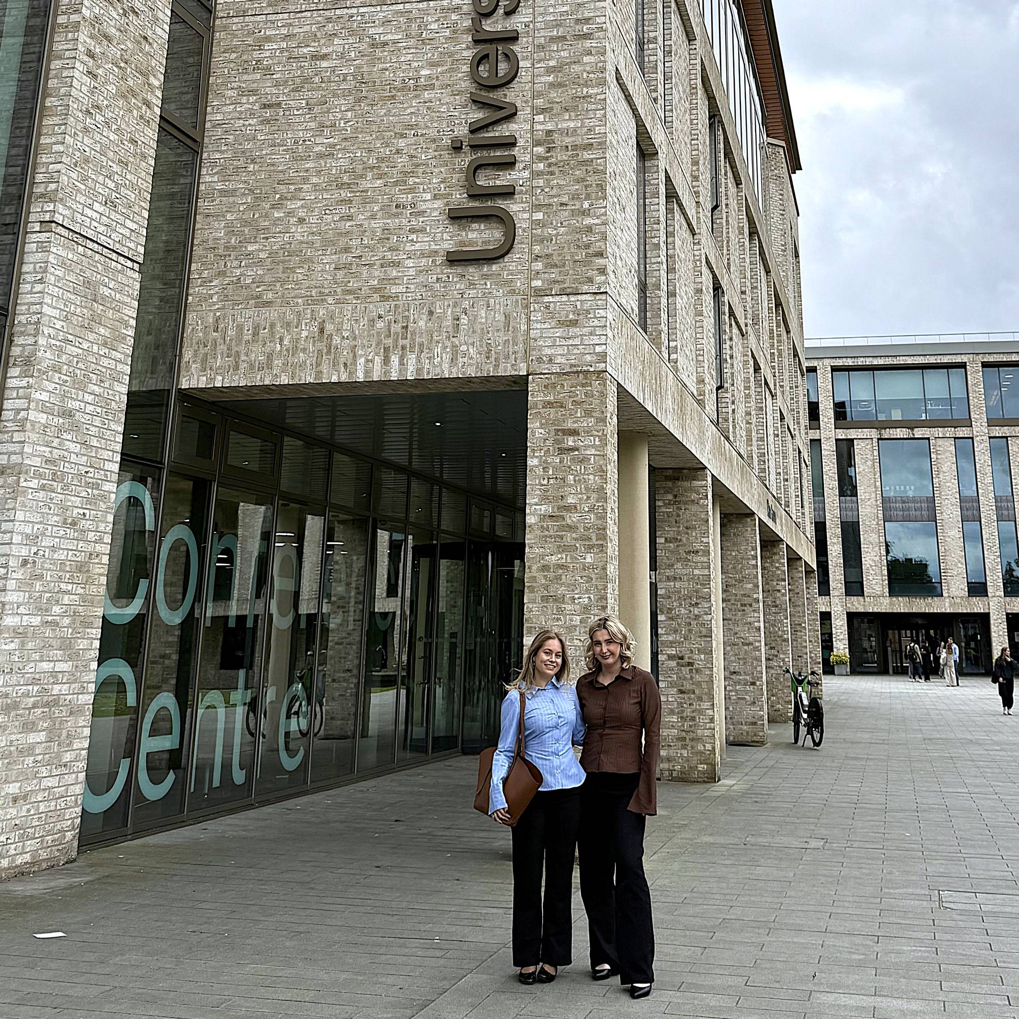 To unge, kvinnelige studenter ved en bygning