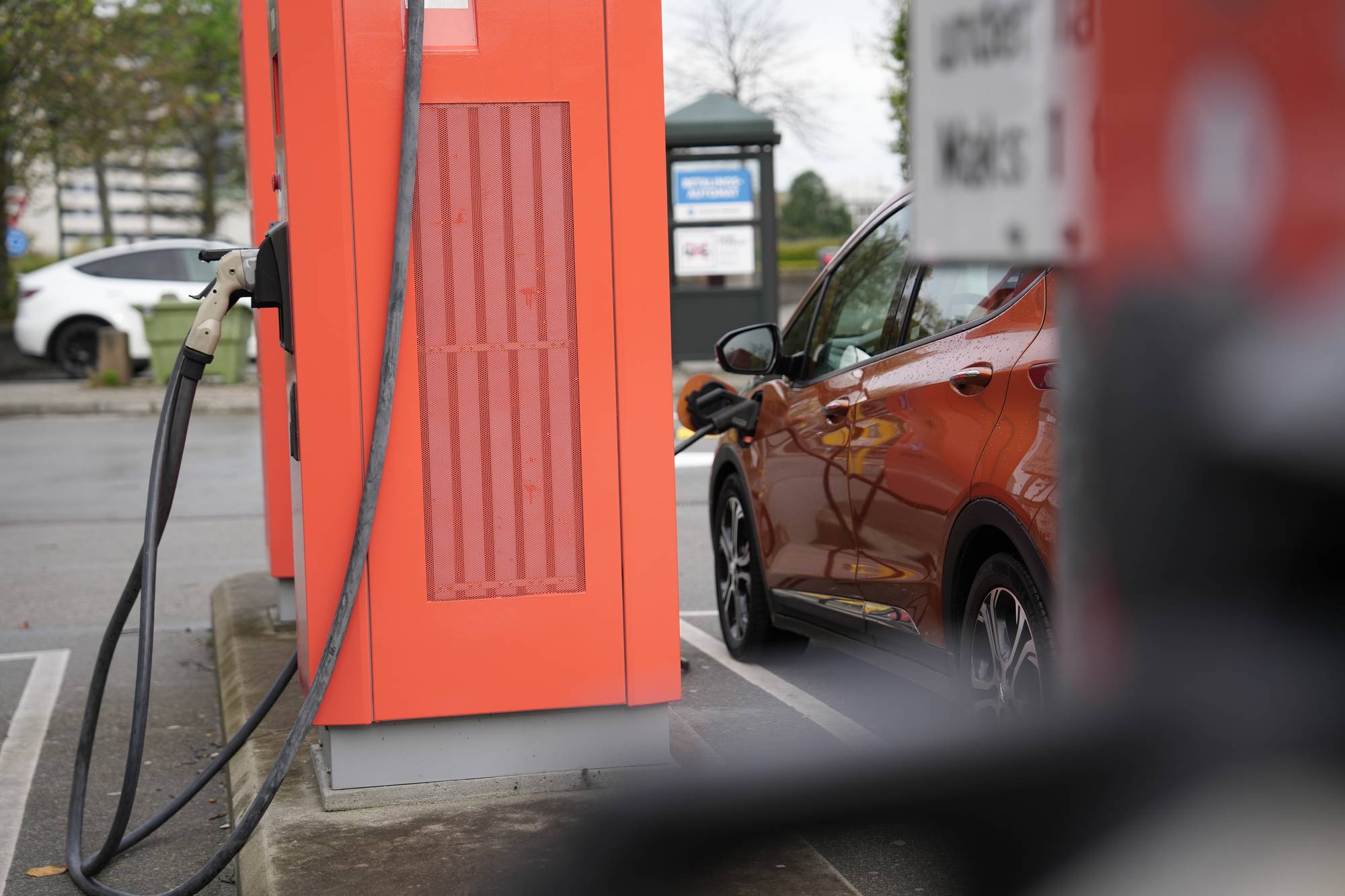 En oransje elbil lades ved en ladestasjon utendørs. (Bildebeskrivelsen er laget av en KI-tjeneste)
