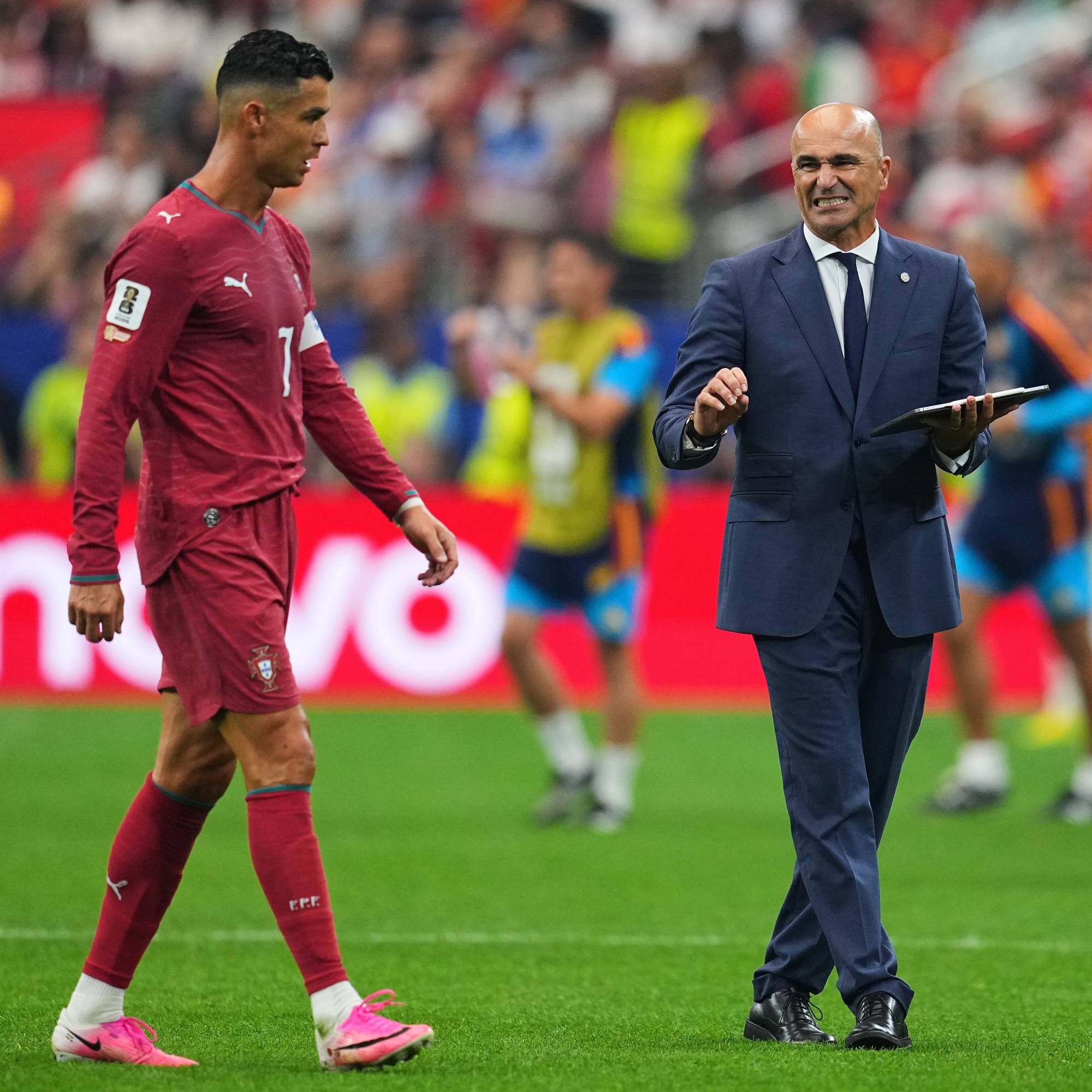 Cristiano Ronaldo går forbi landslagstrener Roberto Martinez på en fotballbane. (Bildebeskrivelsen er laget av en KI-tjeneste)