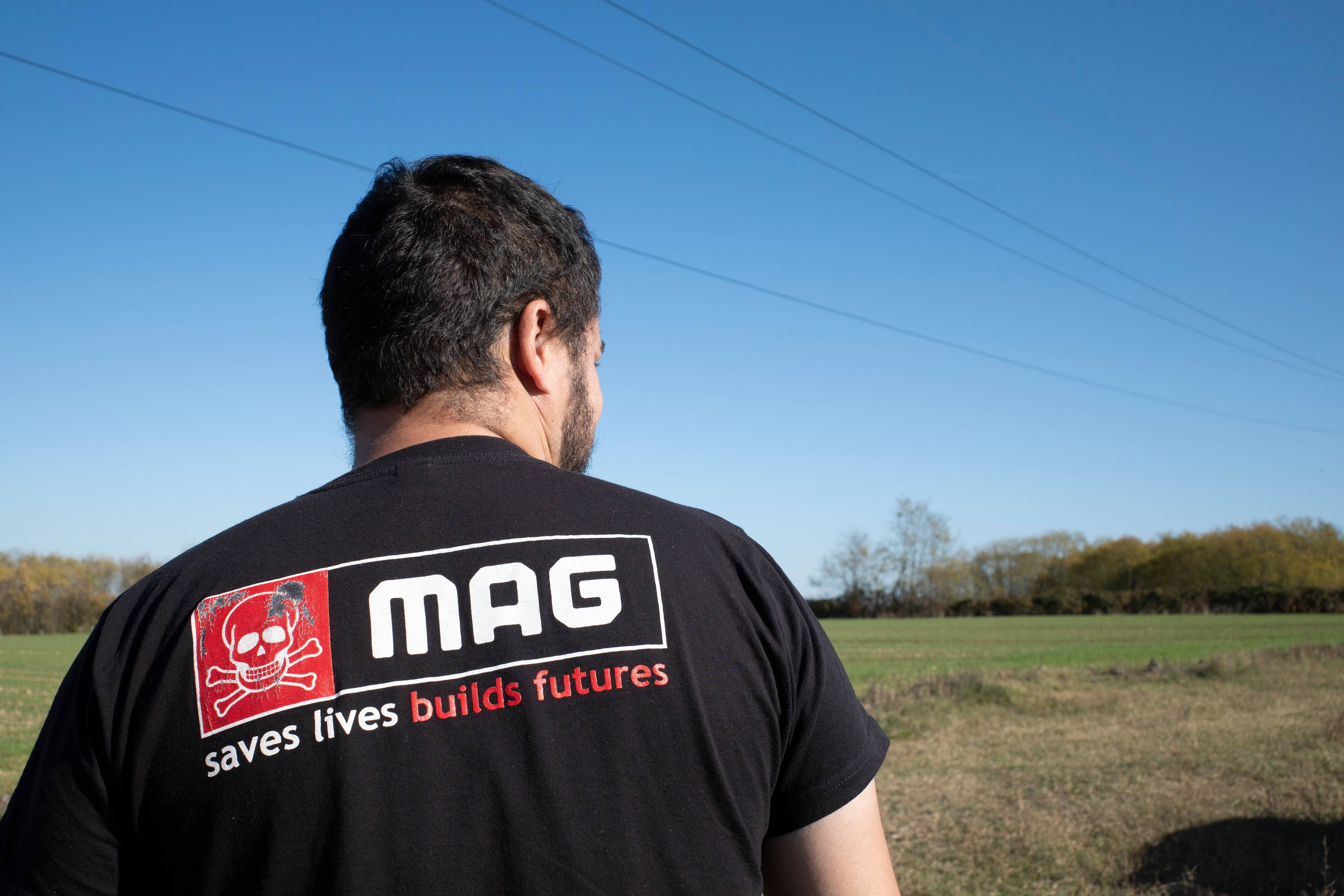 En mann iført svart skjorte ser utover en åker. Det står MAG - saves lives. Builds futures.