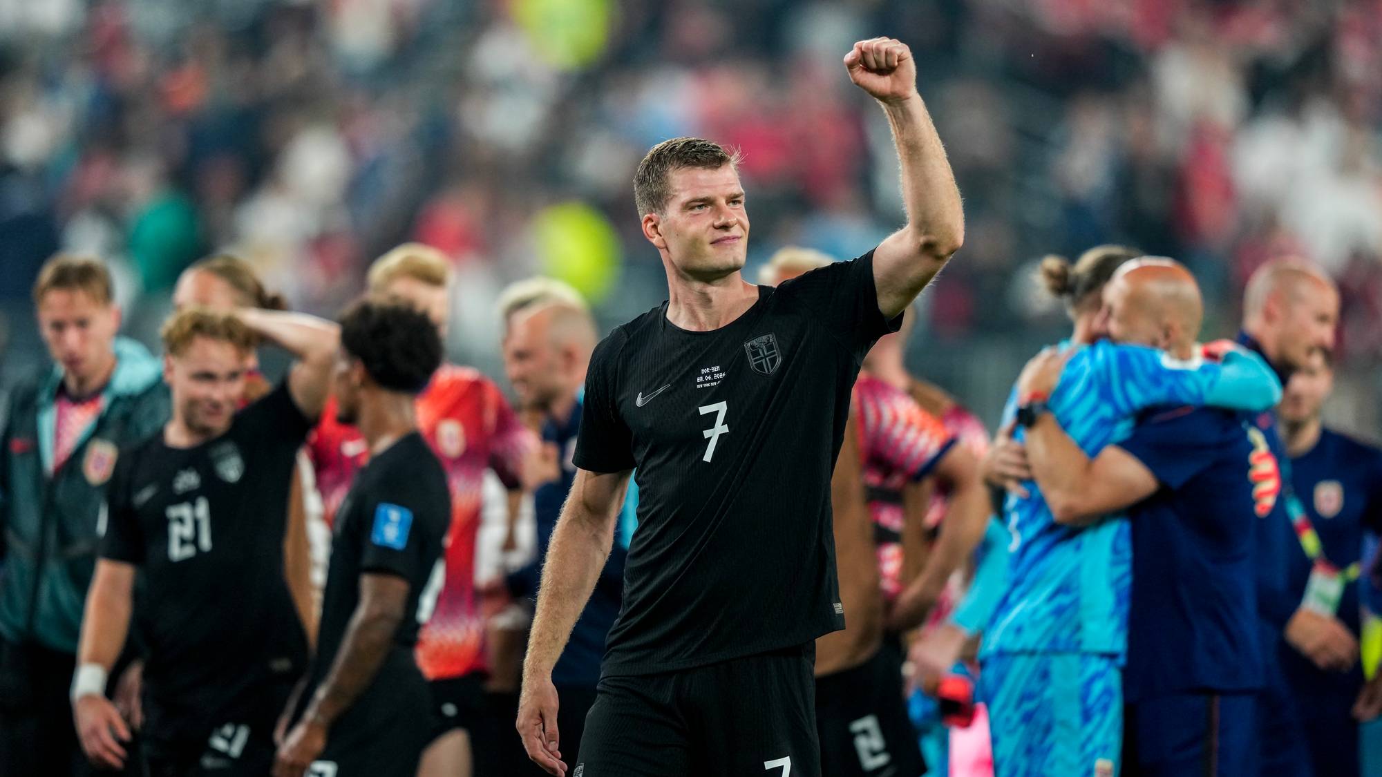 En fotballspiller feirer med knyttneven i været. Han står foran andre spillere på et stadion. Publikumet er uskarpt i bakgrunnen. Fotballspilleren har et nummer 7 på drakten. (Bildebeskrivelsen er laget av en KI-tjeneste)