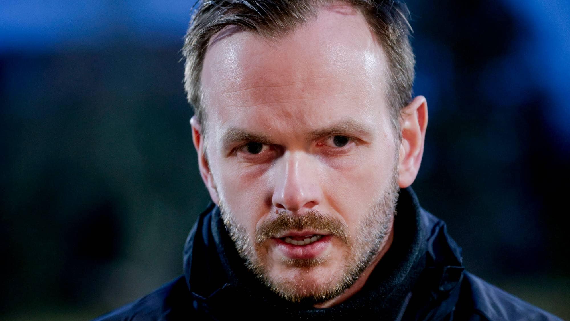 Portrett av en mann med kort hår og skjegg, kledd i en mørk jakke. (Bildebeskrivelsen er laget av en KI-tjeneste)