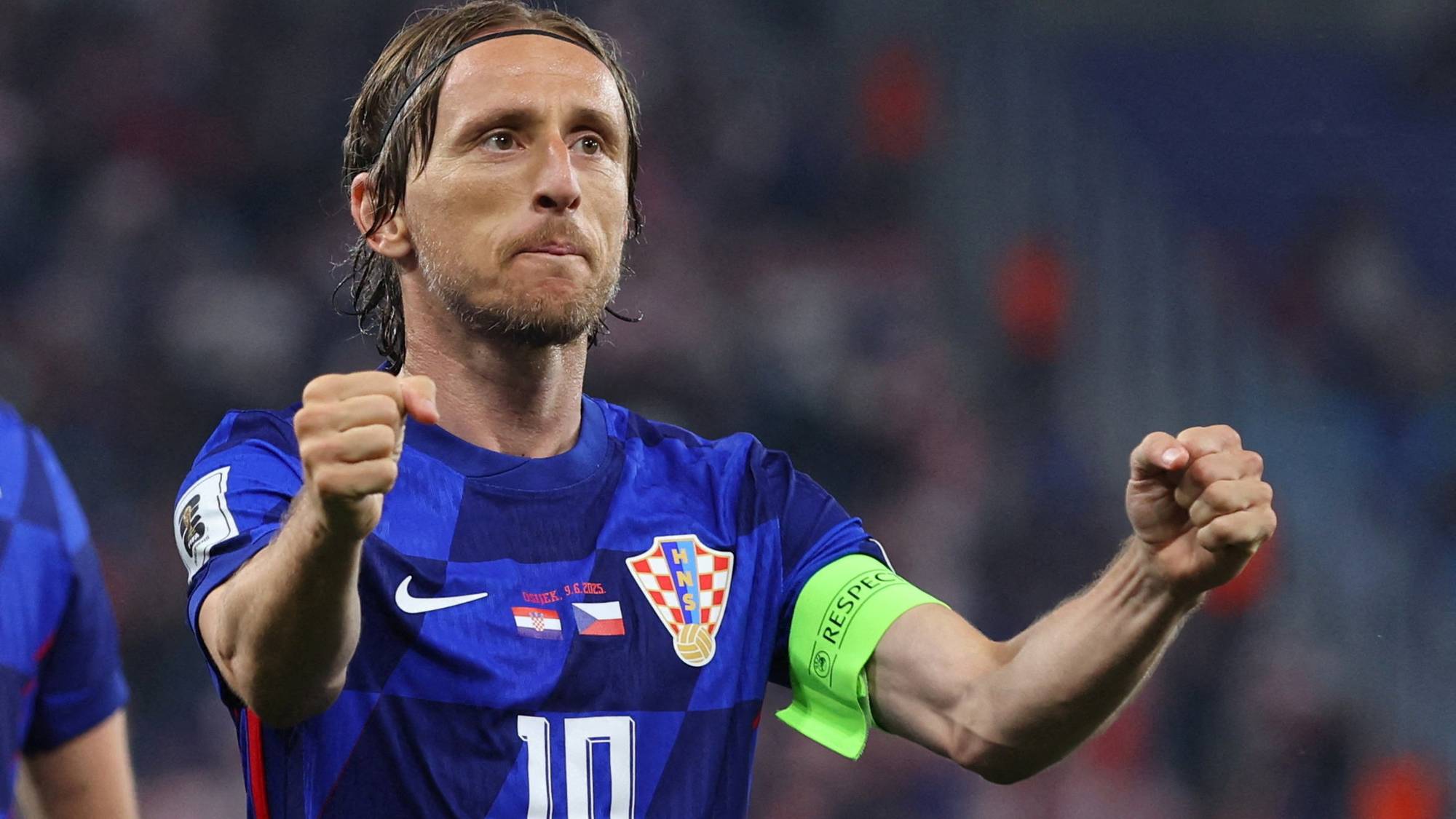 Luka Modrić feirer mens han holder hendene i været. Han spiller i en blå trøye med nummer 10. En grønn armbind med ordet "RESPECT" er synlig på armen. (Bildebeskrivelsen er laget av en KI-tjeneste)