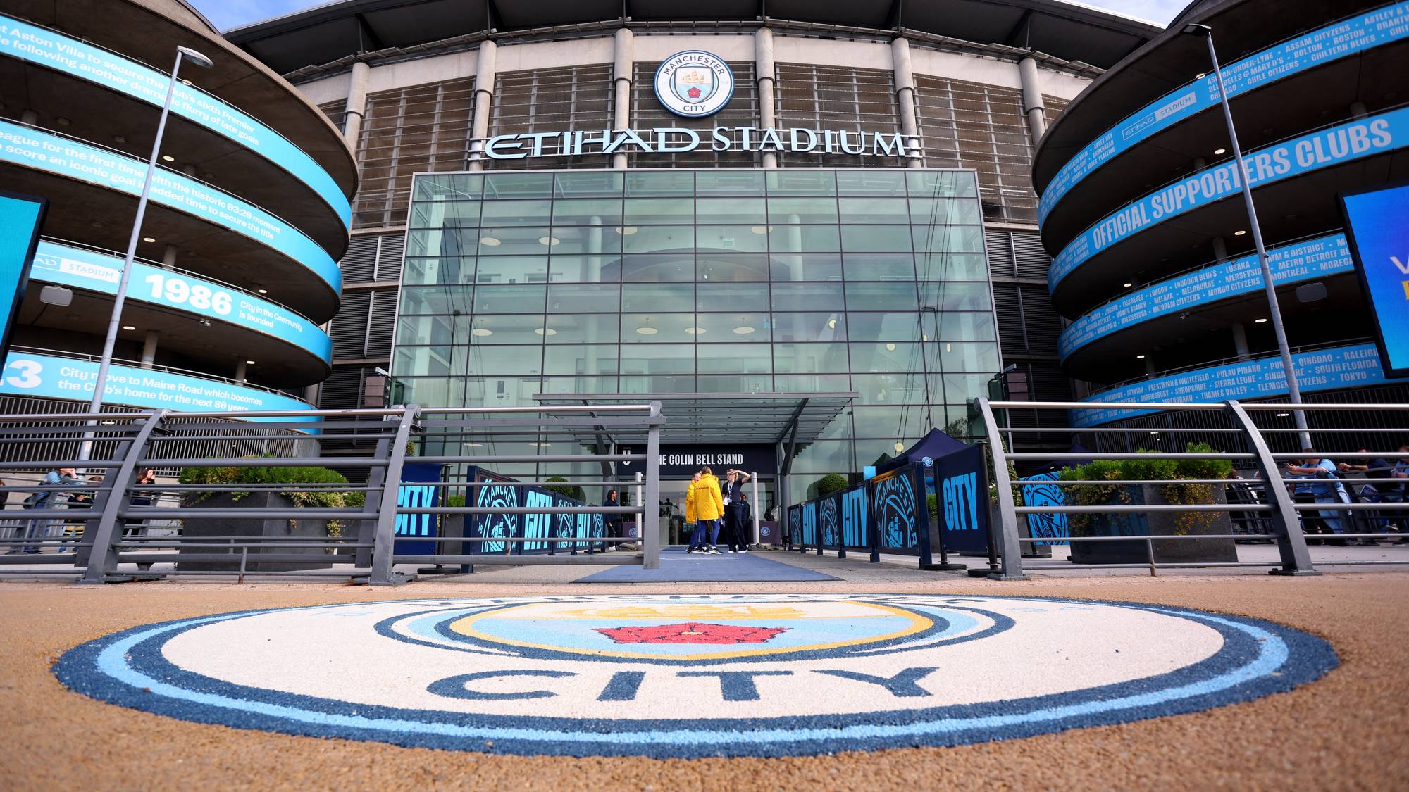 Eksteriør av Etihad Stadium i Manchester med klubbens logo i forgrunnen. (Bildebeskrivelsen er laget av en KI-tjeneste)