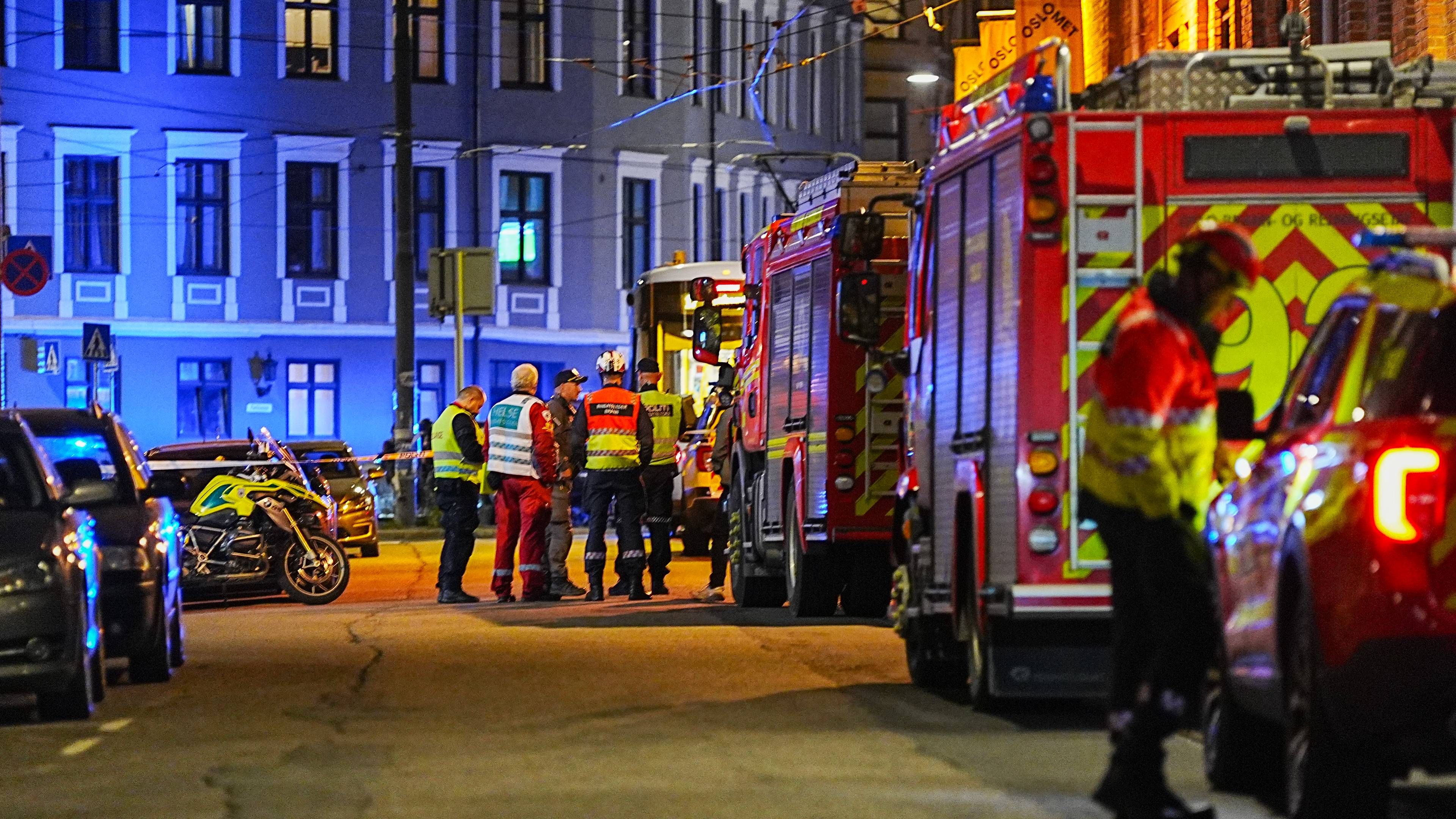 en gruppe nødpersonell som står ved siden av flere brannbiler. Det er masse blålys i bakgrunnen.